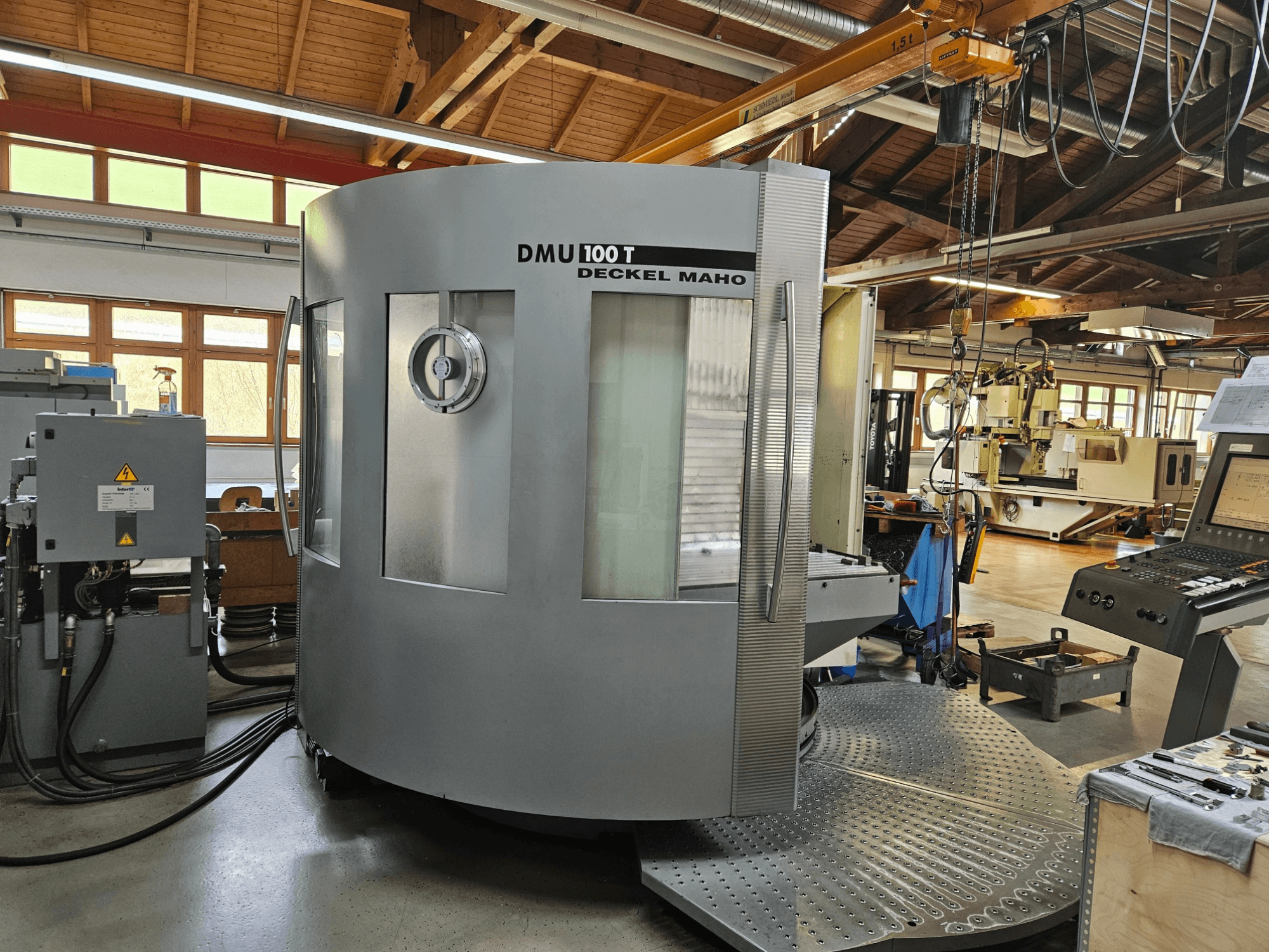 Stroj DMU 100 T Deckel Maho CNC při pohledu zepředu, s velkou kruhovou základnou, ovládacím panelem a skleněným krytem.