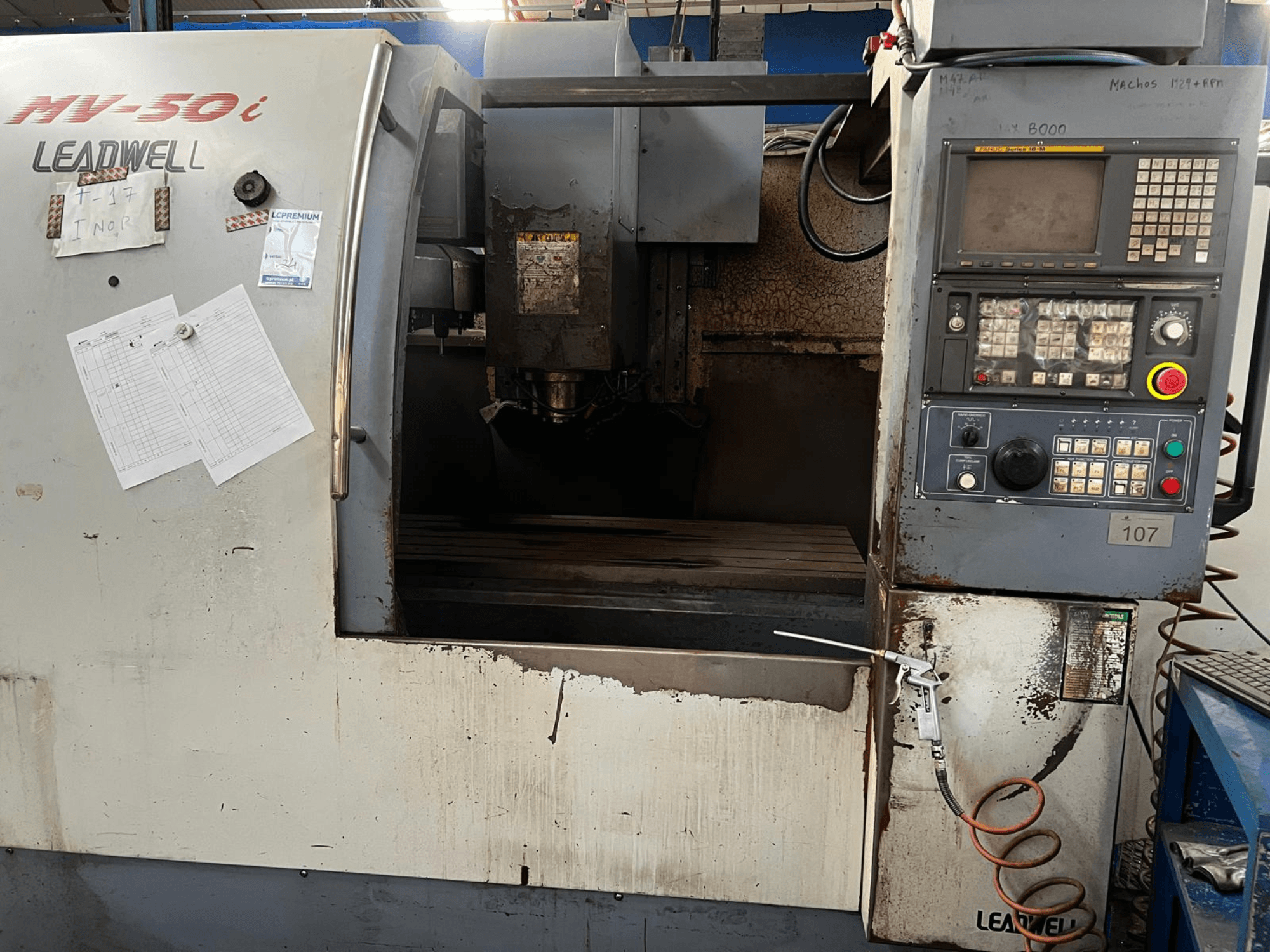 Vertikální obráběcí centrum Leadwell MV-50i, pohled zepředu, na kterém je vidět ovládací panel, oblast vřetena a pracovní stůl s známkami opotřebení.