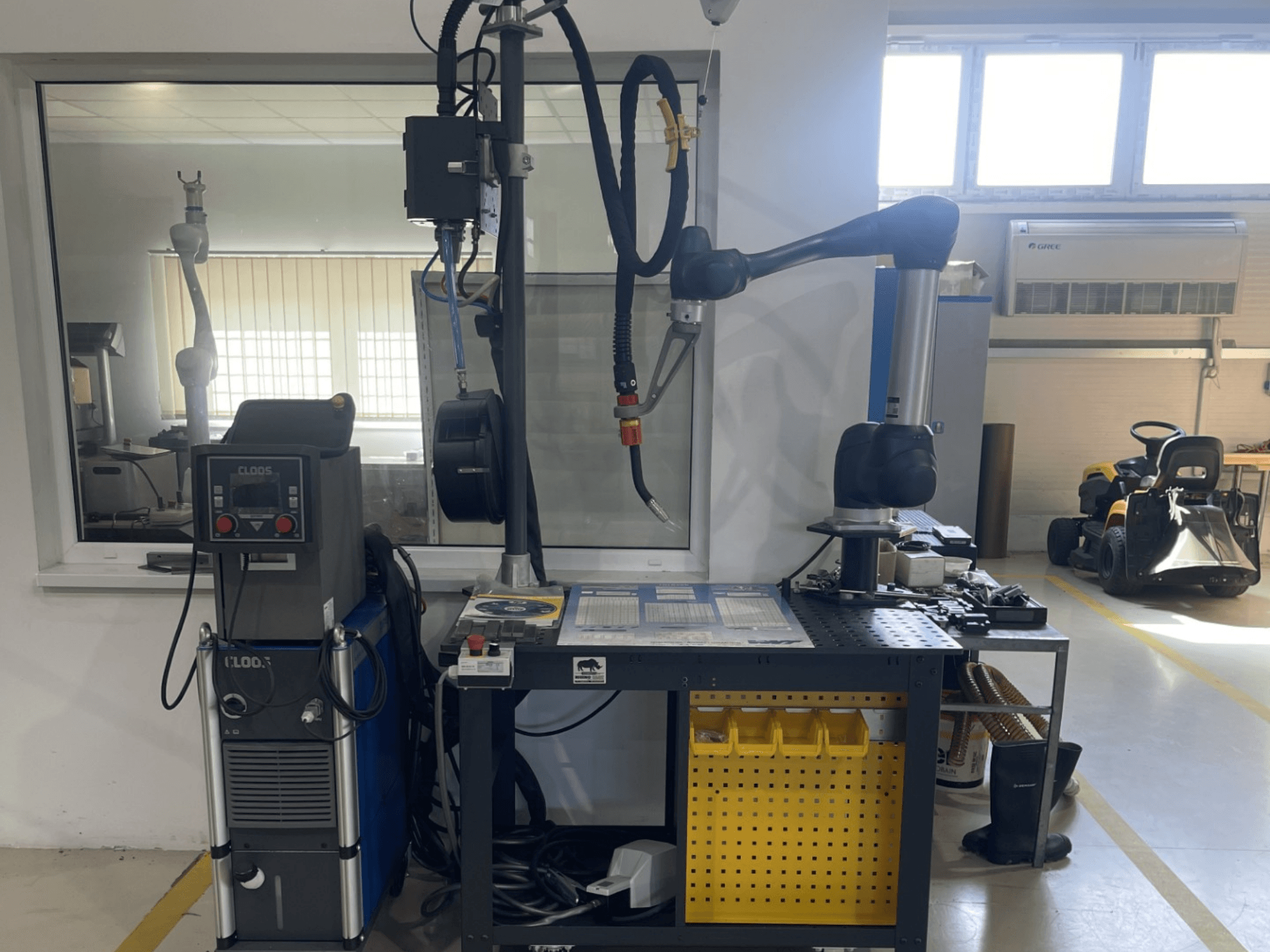 Kolaborativní robot DOOSAN M1013 v dílně, boční pohled se svařovacím zařízením a nářadím na pracovním stole.