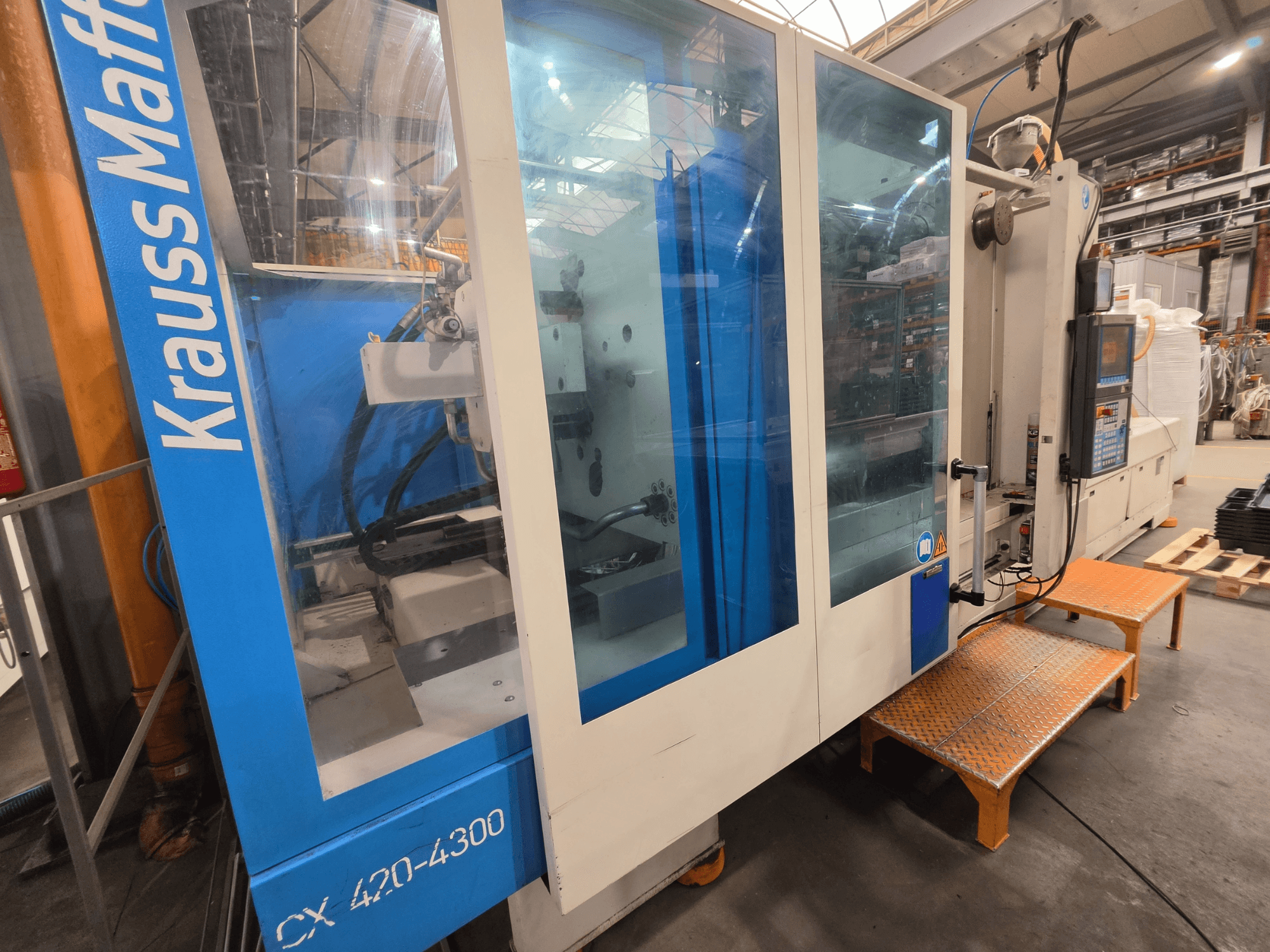 Hydraulický vstřikovací stroj Krauss Maffei CX 420-4300, boční pohled, zobrazující ovládací panel a průhledné panely.