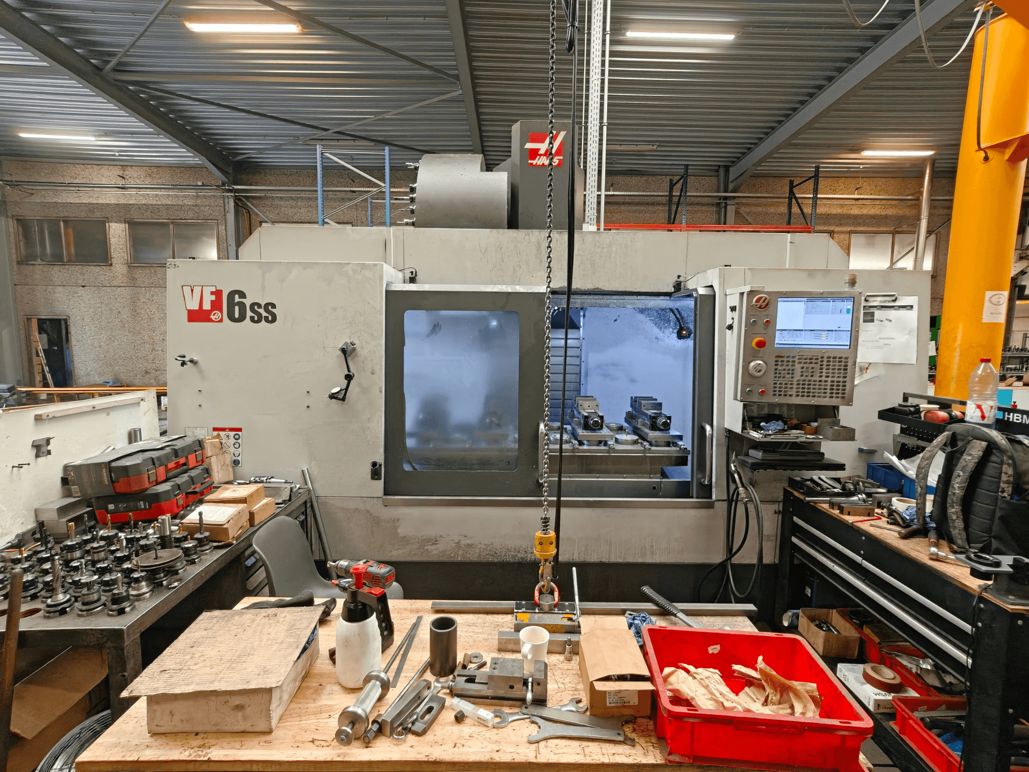 Vertikální obráběcí centrum Haas VF-6SS v dílně, boční pohled znázorňující ovládací panel a pracovní prostor zaplněný nástroji.