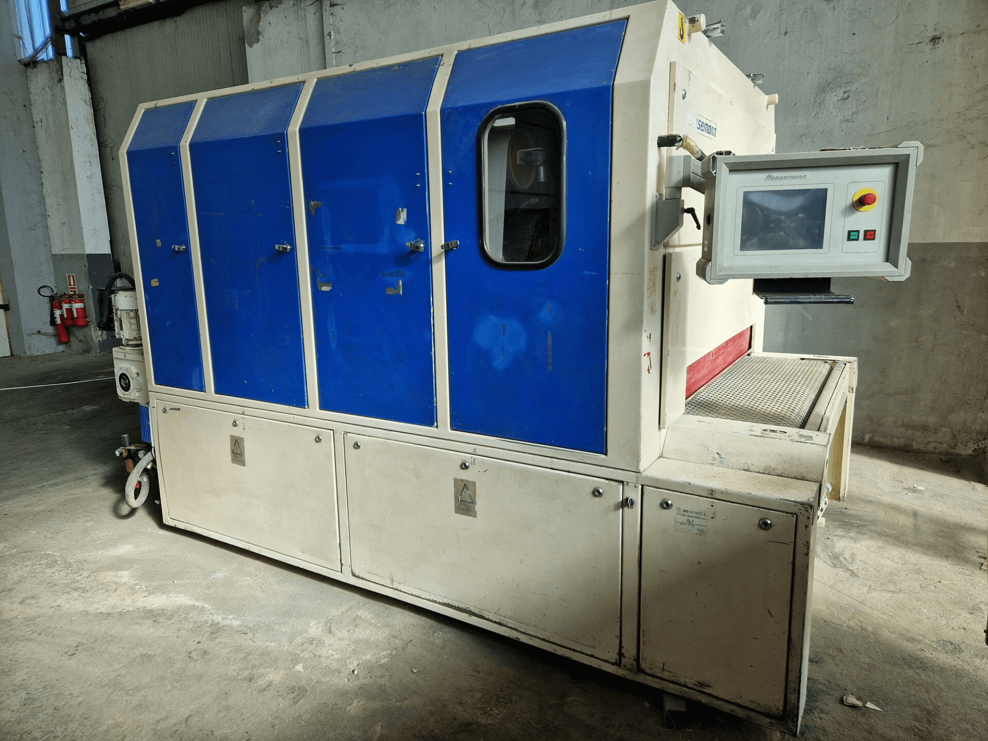 Průmyslový stroj značky "Sedecom", boční pohled; modré panely, ovládací obrazovka a strukturovaný povrch pro manipulaci s výrobky.