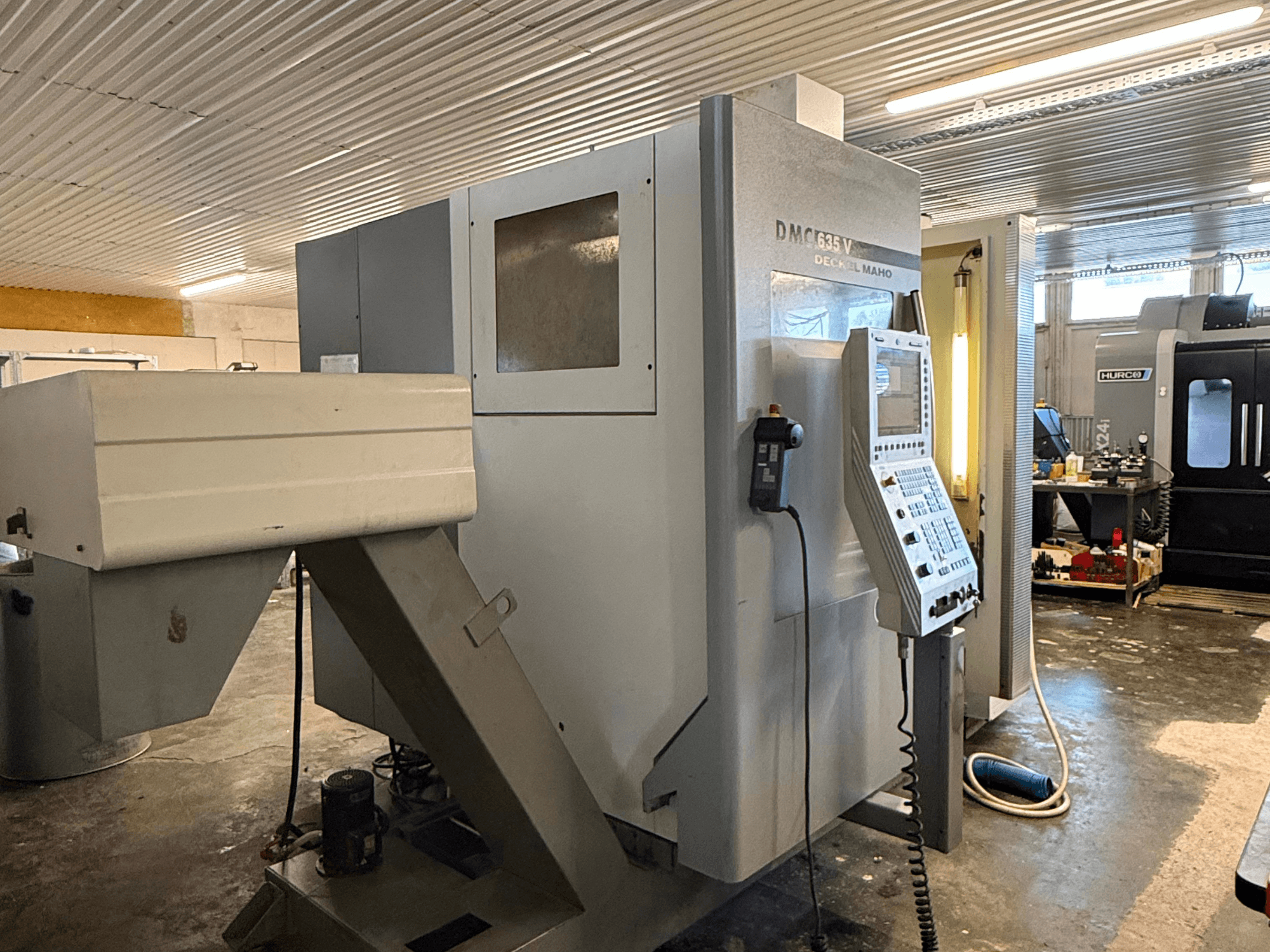 Frézka DMC G635V v dílně, pohled zepředu s viditelným ovládacím panelem a připojenými elektrickými nástroji.