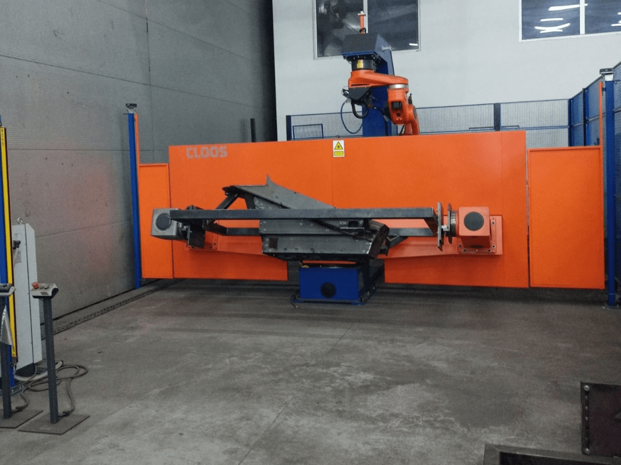 Pohled zepředu na automatizační systém CLOOS QIROX QRC-350-E s robotickým ramenem a kovovou konstrukcí v průmyslovém prostředí.