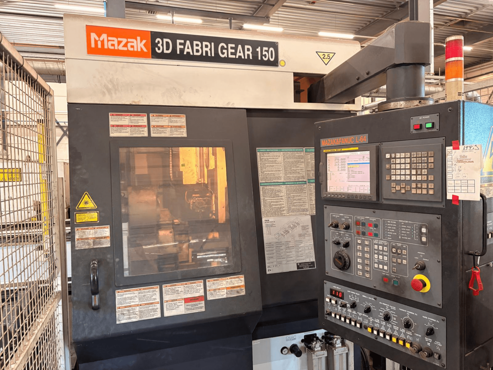 Stroj na řezání trubek Mazak 3D Fabri Gear 150, pohled zepředu znázorňující ovládací panel, bezpečnostní štítky a uživatelské rozhraní.