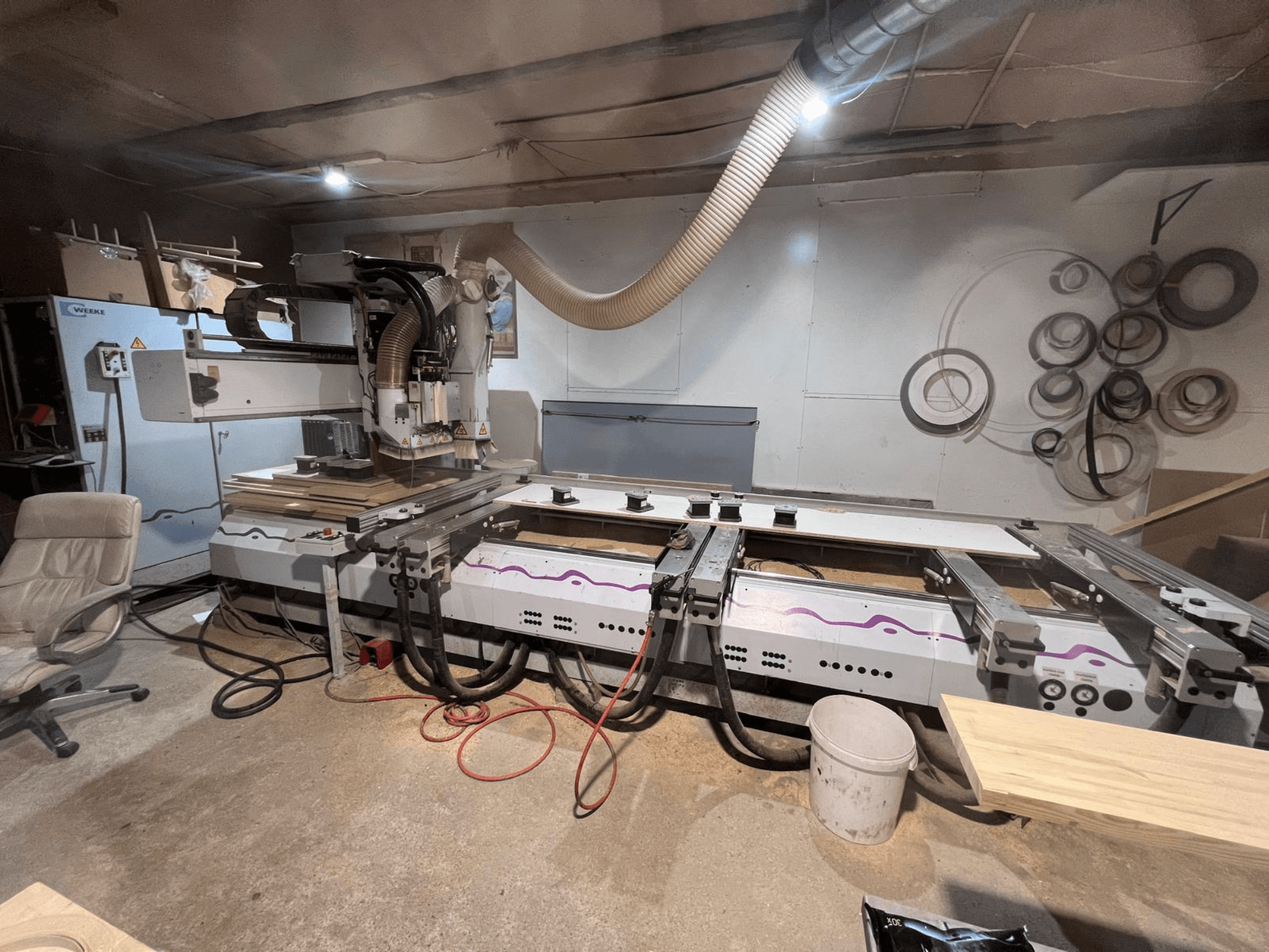 CNC dřevoobráběcí centrum Weeke OPTIMAT BP 120 v dílně, pohled zepředu s kusy dřeva a nástroji viditelnými na pracovní ploše.