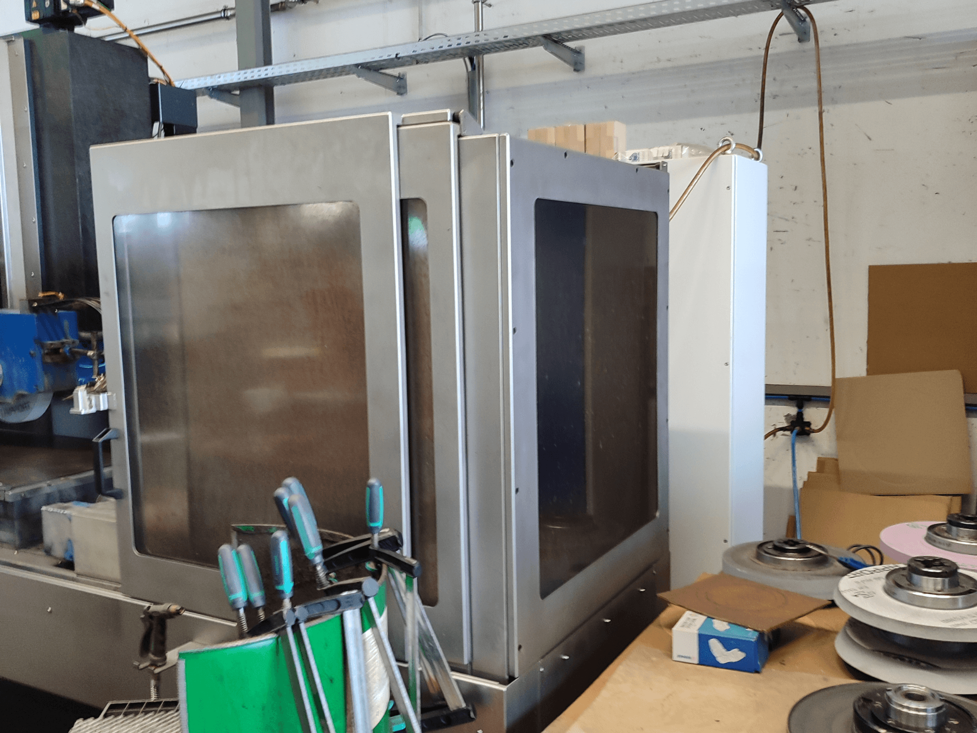 Povrchová bruska HEINZ STÖCKEL FD 1560 NC-T, boční pohled na kovový plášť a brusné komponenty v dílenském prostředí.