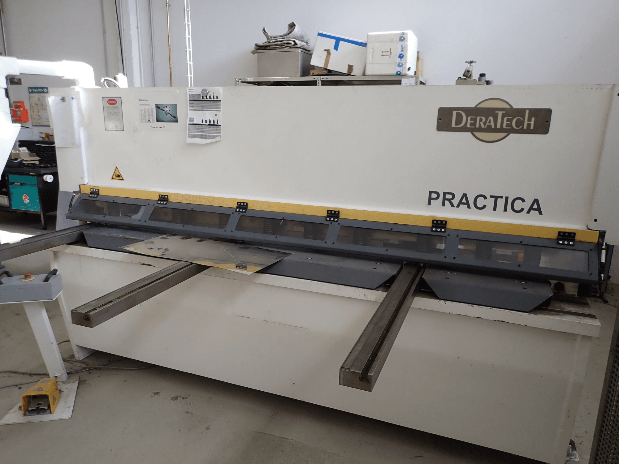 CNC stříhací stroj DERATECH Practica, pohled zepředu, řezací nůž a plechy na pracovní ploše.