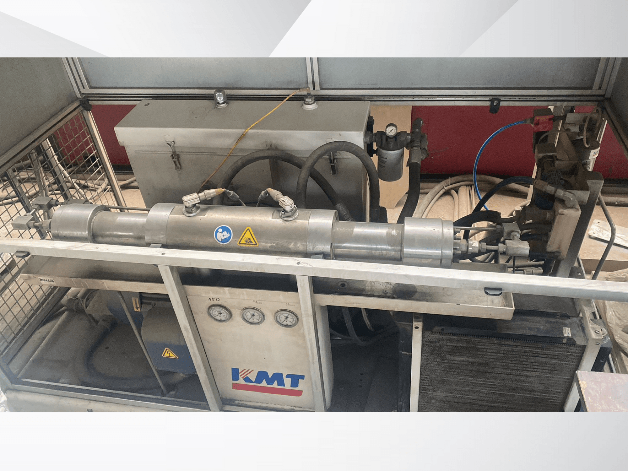 Hydraulický stroj KMT v čelním pohledu, s manometry, hadicemi a kovovým krytem, ideální pro průmyslové aplikace.