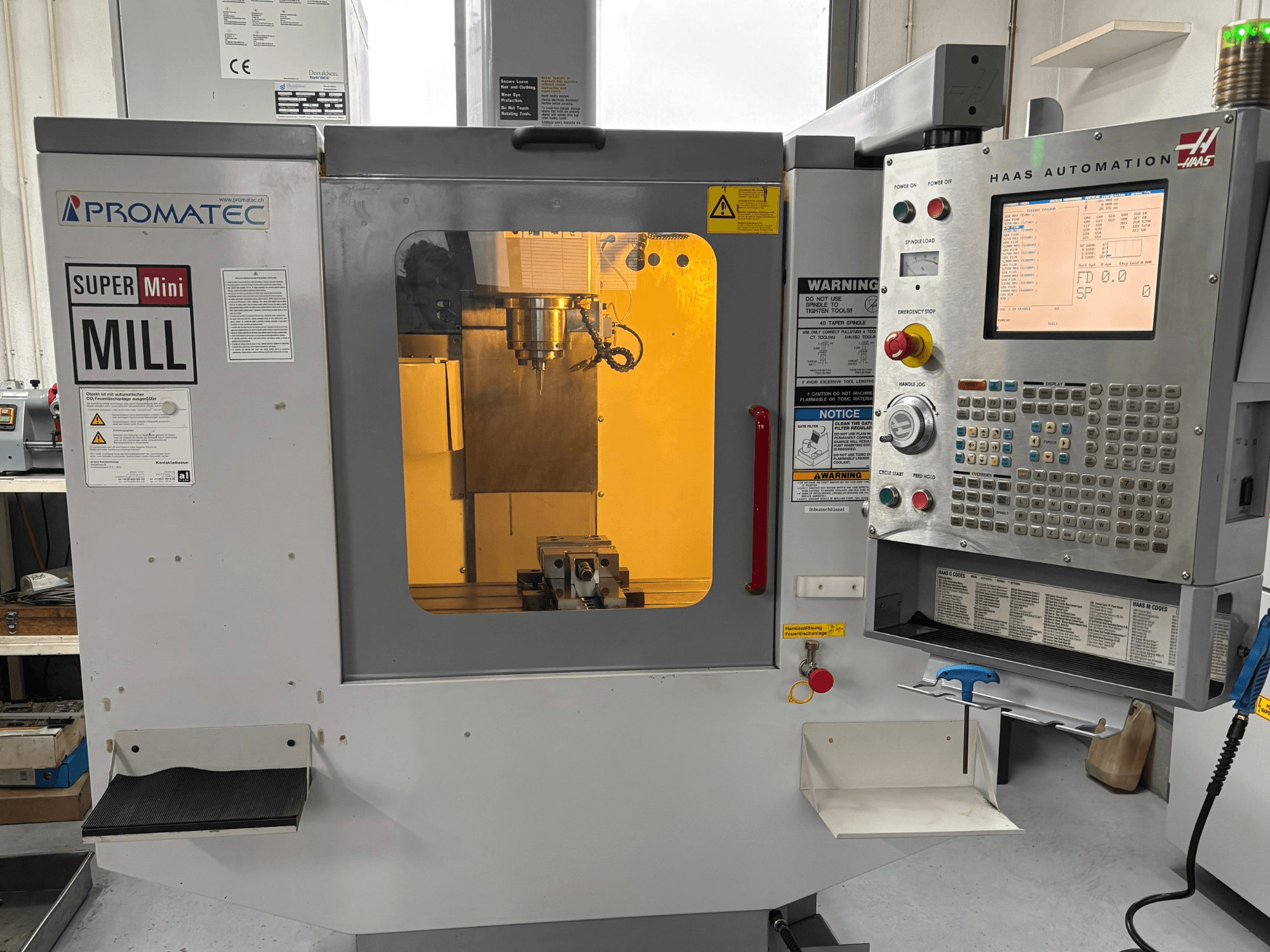 Frézka Promatec Super Mini Mill v čelním pohledu, vybavená ovládacím panelem Haas Automation a viditelným řezným nástrojem uvnitř.