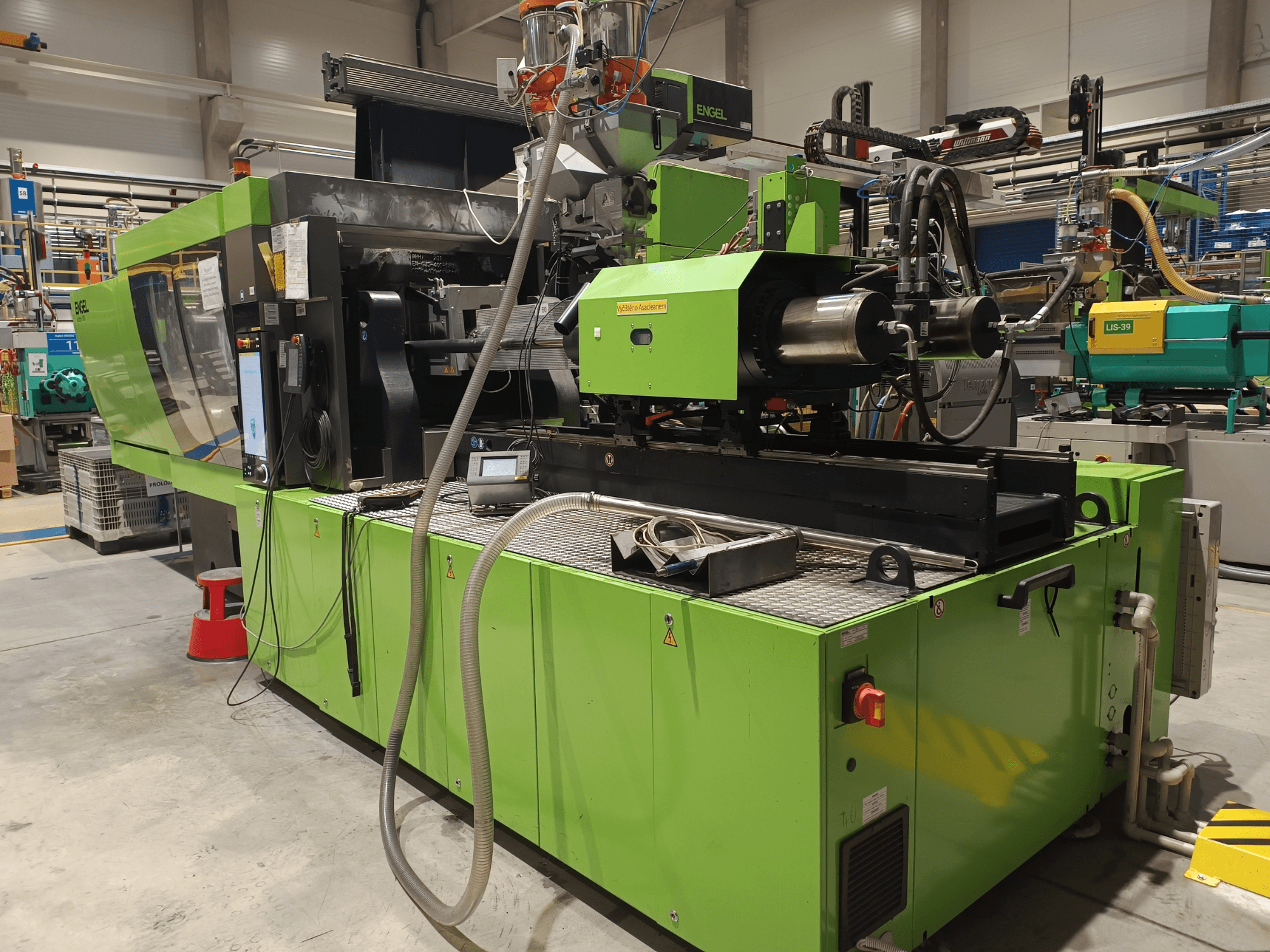 Vstřikovací stroj Engel, boční pohled, zelený exteriér, s viditelným panelem s dotykovou obrazovkou a hydraulickými komponenty.