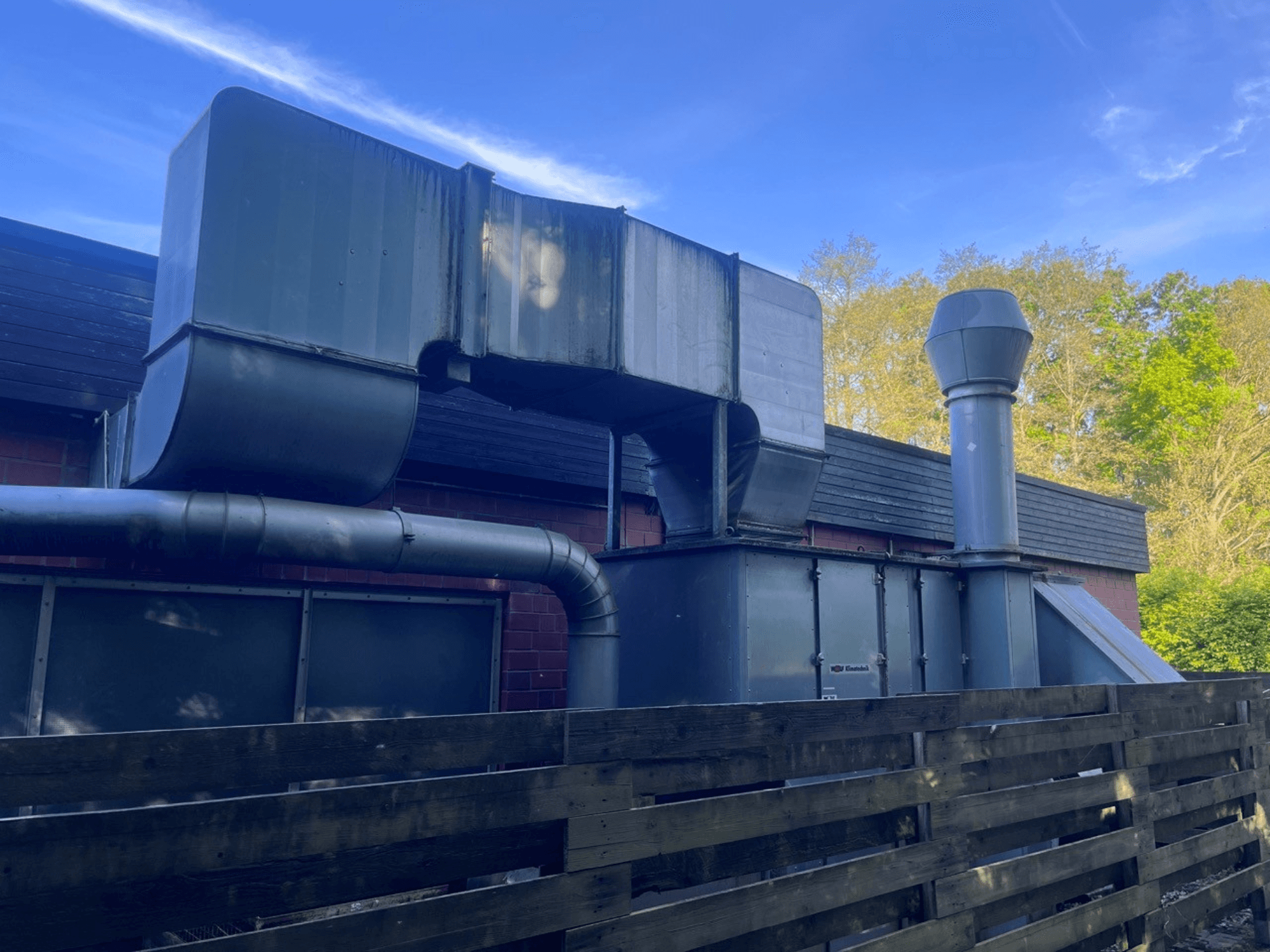 Průmyslový ventilační systém s kovovým potrubím, boční pohled; obsahuje čtvercový a válcový komín, zelená barva.