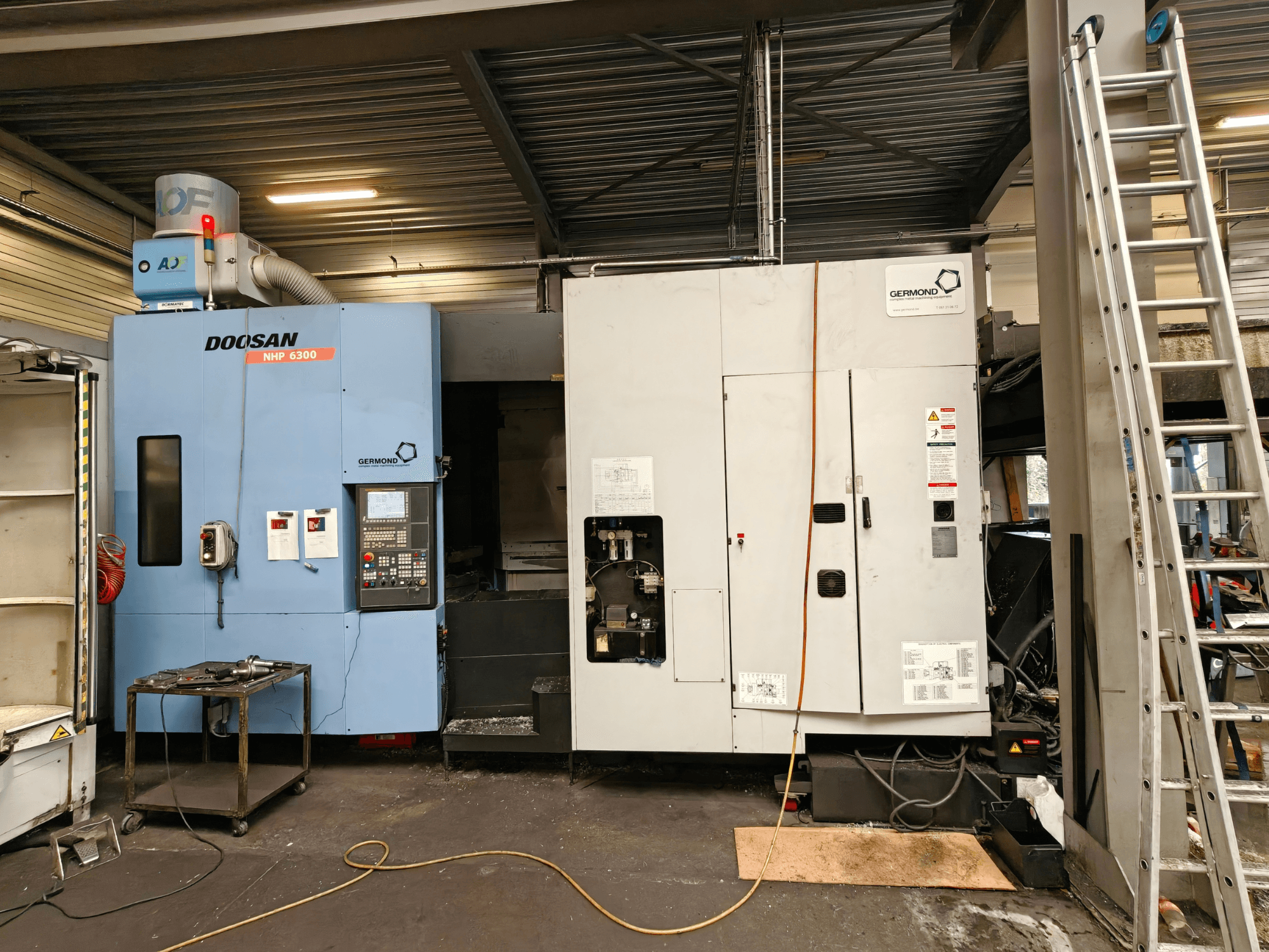 Horizontální obráběcí centrum DOOSAN NHP6300 v čelním pohledu, na kterém je vidět ovládací panel a sousední stroje v prostředí dílny.