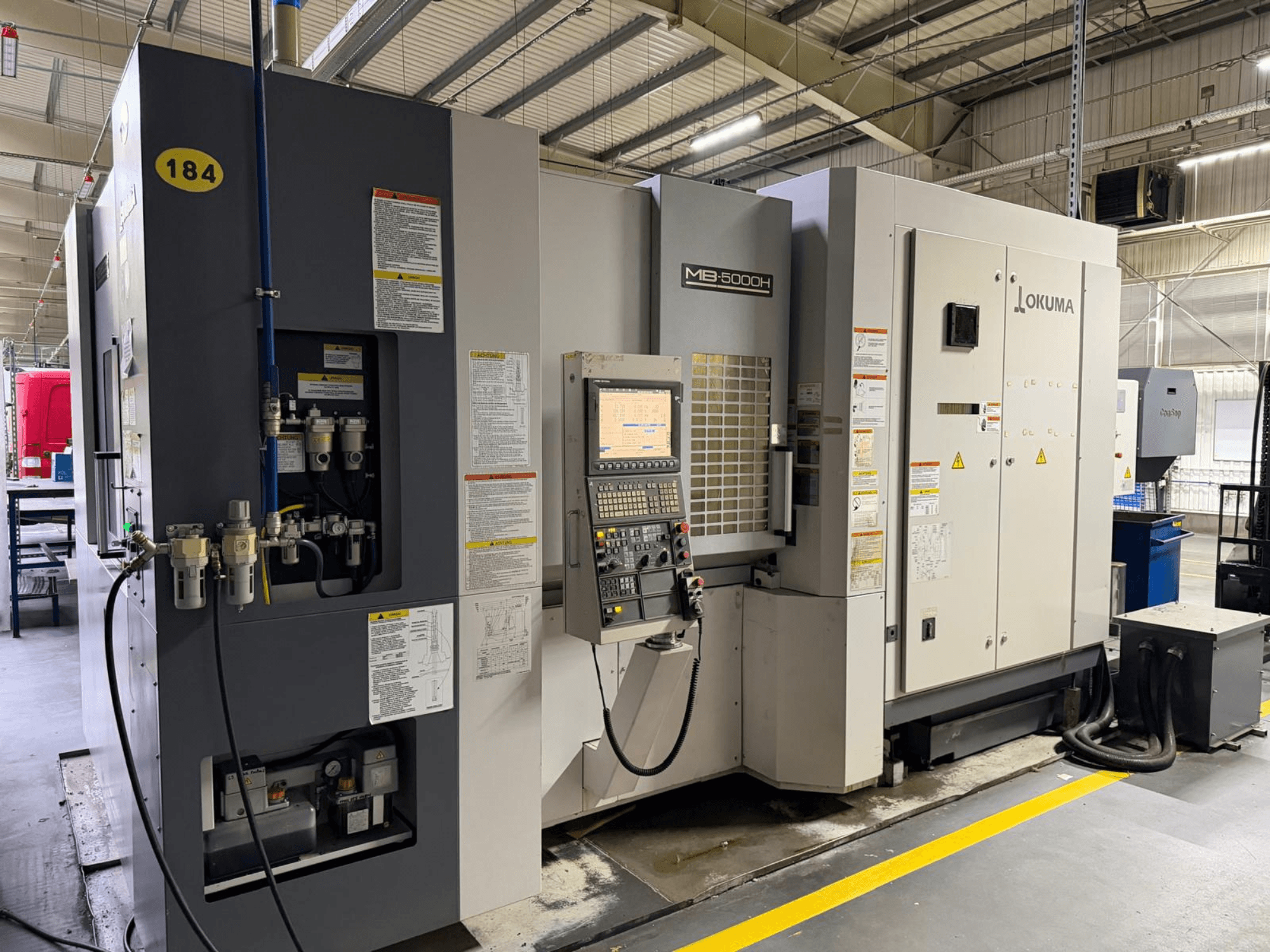 Horizontální obráběcí centrum Okuma MB 5000H z čelního pohledu, s ovládacími prvky, označením a hydraulickými přípojkami.