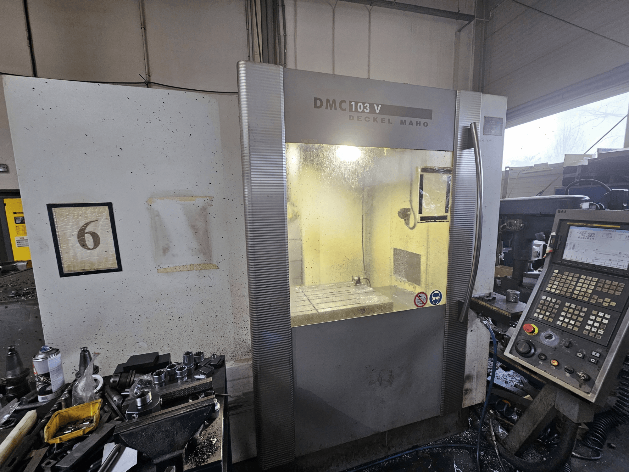 Pohled zepředu na CNC stroj Deckel Maho DMC 103 V, zobrazující ovládací panel, pracovní plochu a číslovaný ukazatel "6".