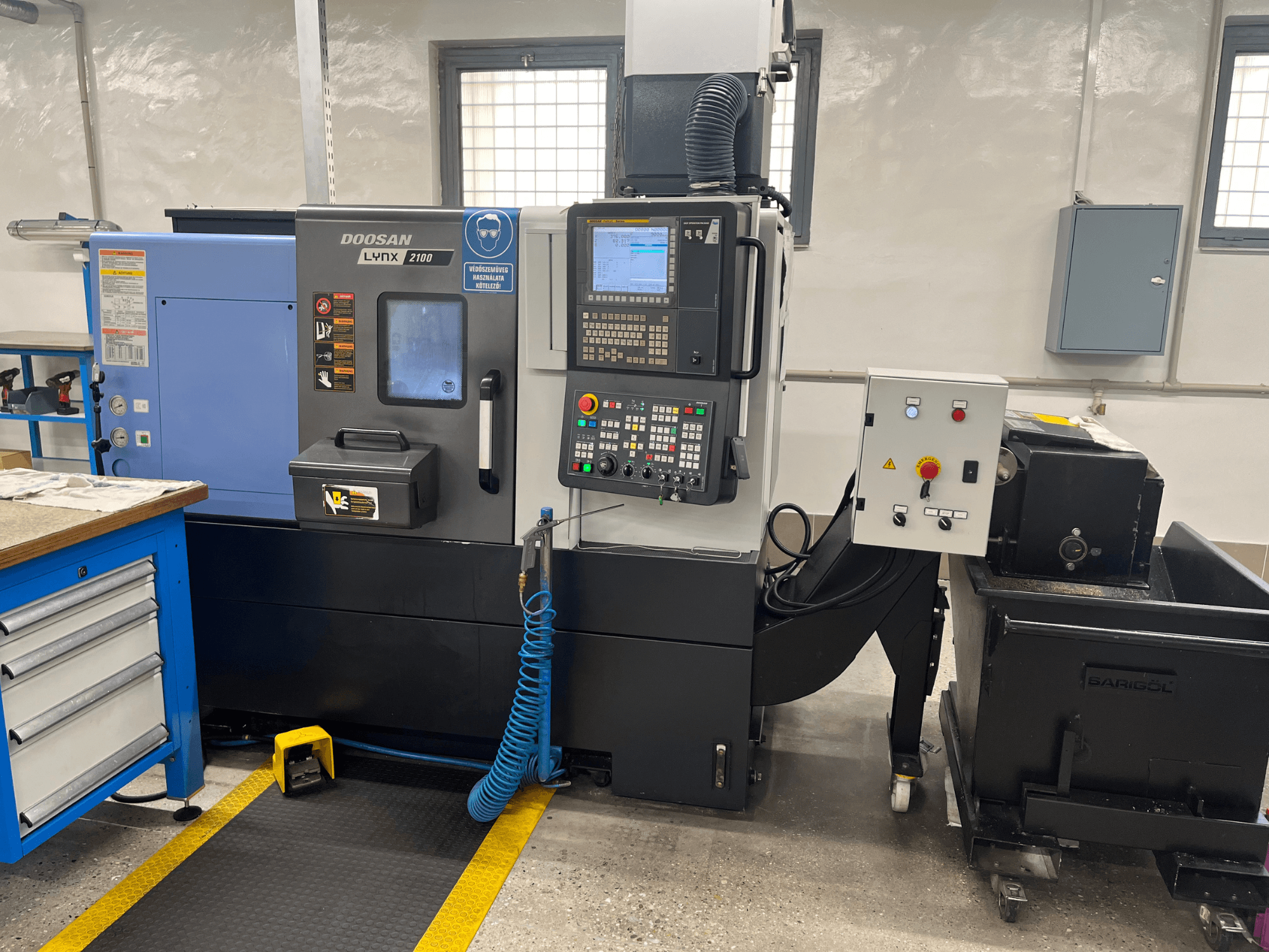 Soustruh Doosan Lynx 210 v dílně, zobrazení ovládacího panelu, úložného prostoru pro nástroje a chladicího systému, boční pohled s detaily pracovního prostoru.