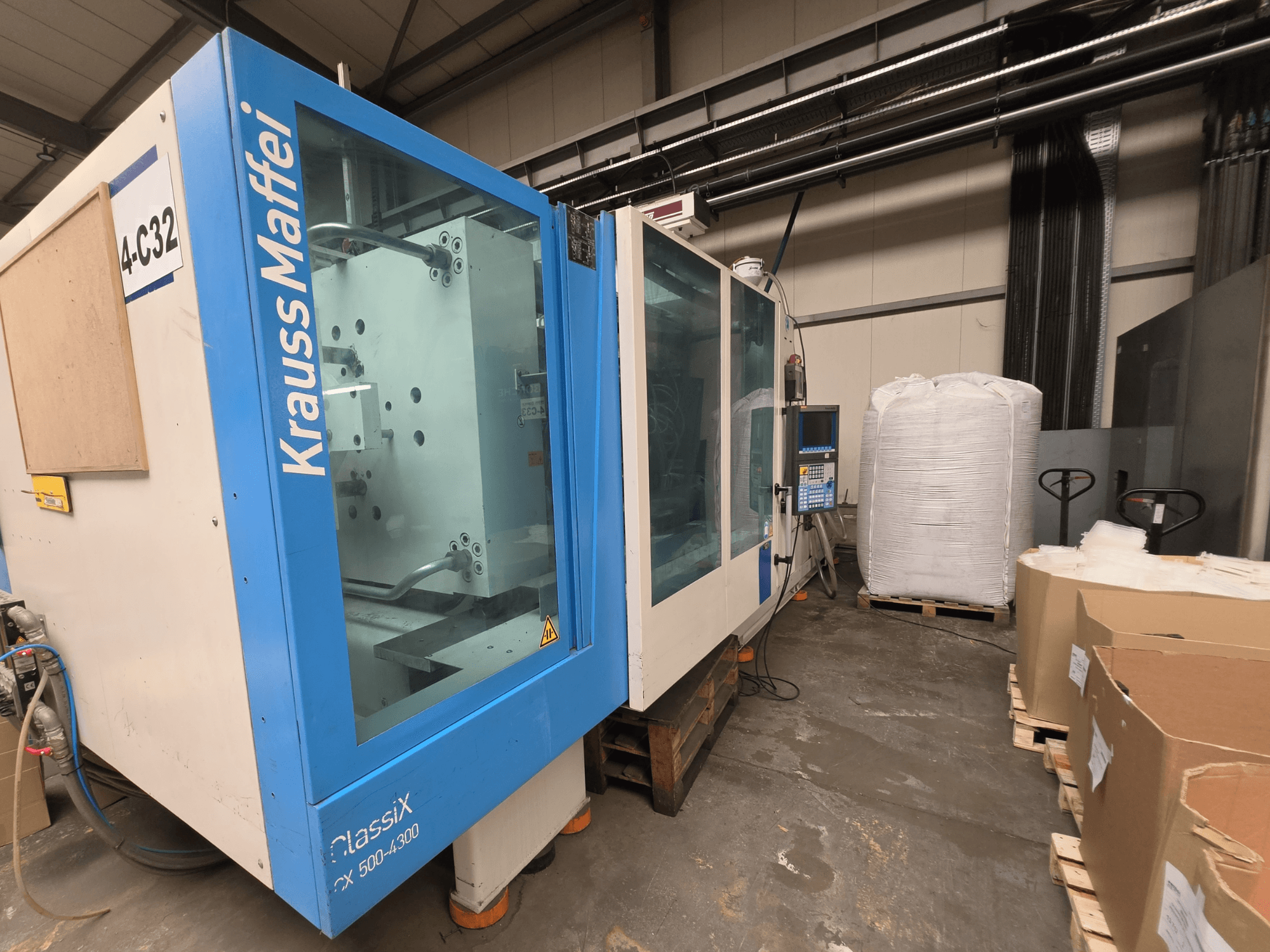 Hydraulický vstřikovací stroj Krauss Maffei 500-4000 CX, boční pohled na ovládací panel a blízké obalové materiály.