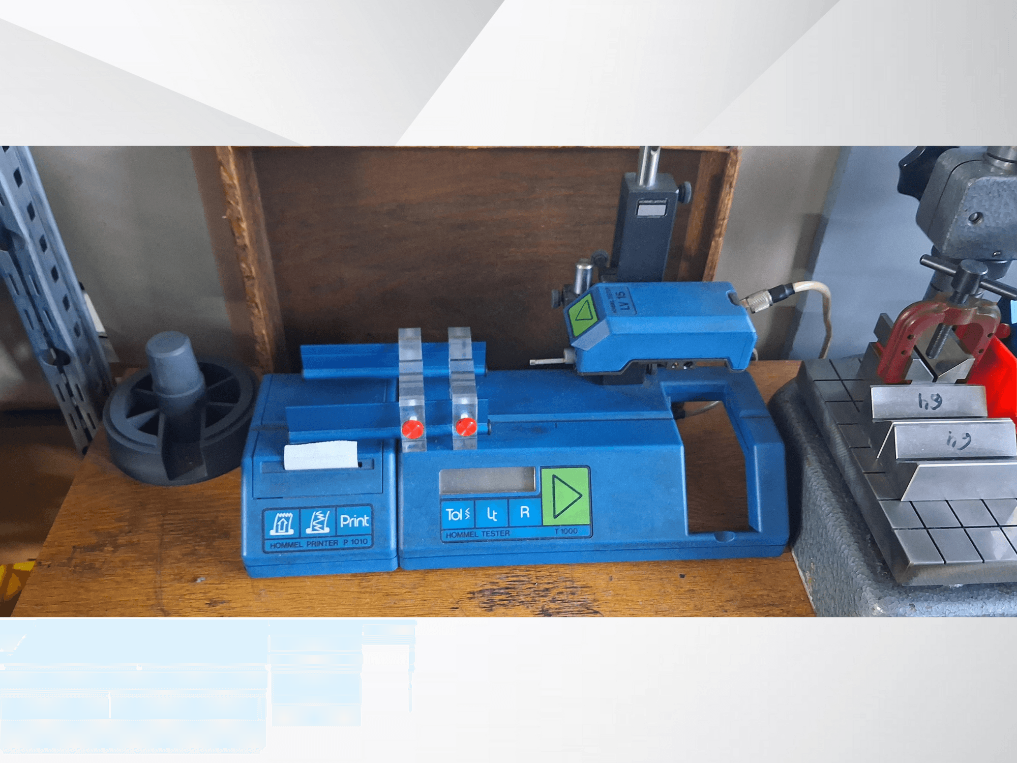 Modrá tiskárna Hommel T 1000 a tester T 1 010 s červenými tlačítky, pohled zepředu na pracovním stole s kovovými bloky.