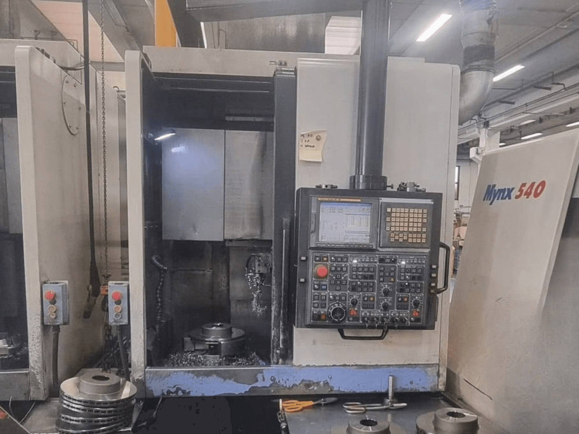 Pohled zepředu na vertikální soustruh DOOSAN PUMA V400-2SP, na kterém je vidět ovládací panel a uspořádání obrobku uvnitř stroje.
