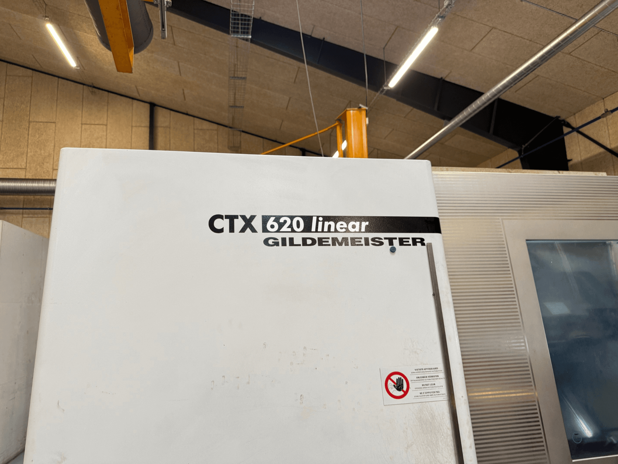 Boční pohled na stroj CTX 620 Linear Gildemeister s bílým vnějším povrchem a bezpečnostními výstražnými štítky.