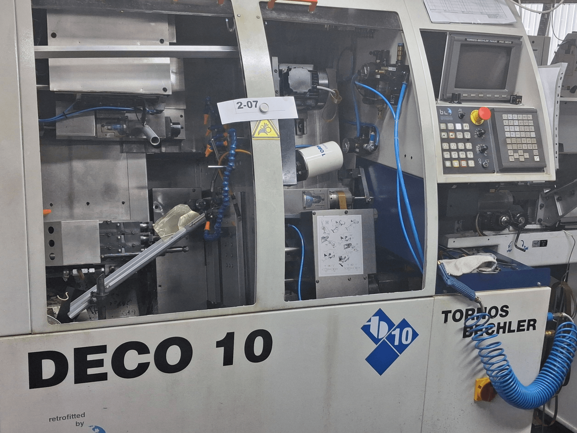 Pohled zblízka na soustruh TORNOS Deco 10a švýcarského typu, který ukazuje vnitřní mechanismus a detaily ovládacího panelu.