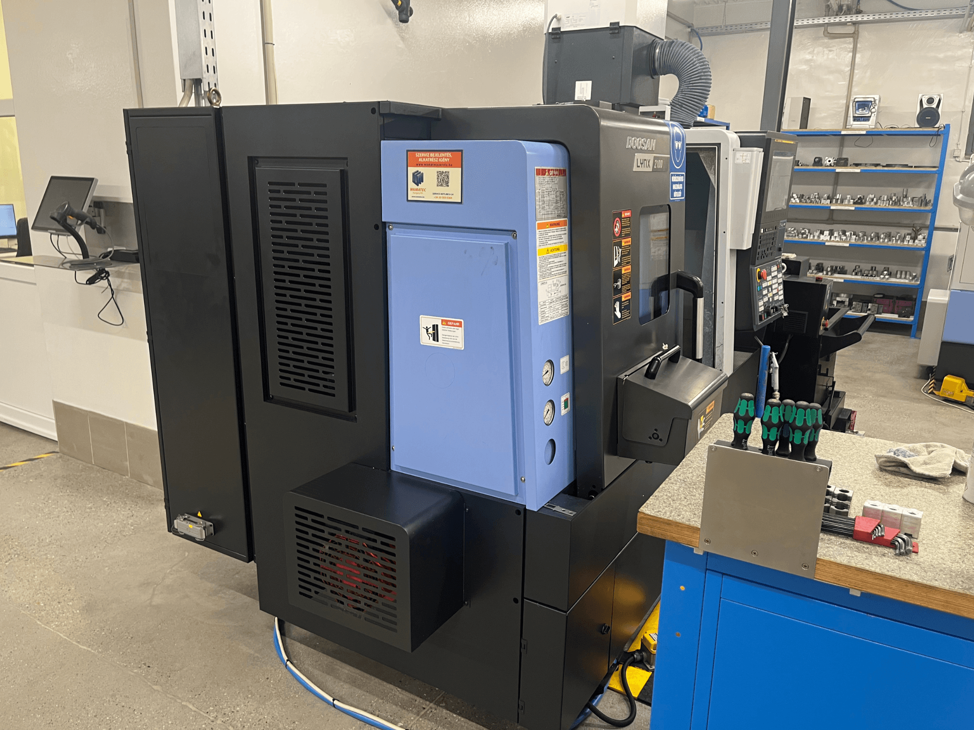 Soustruh Doosan Lynx 2100, boční pohled na ovládací panel, ventilační systém a nástroje na pracovním stole.