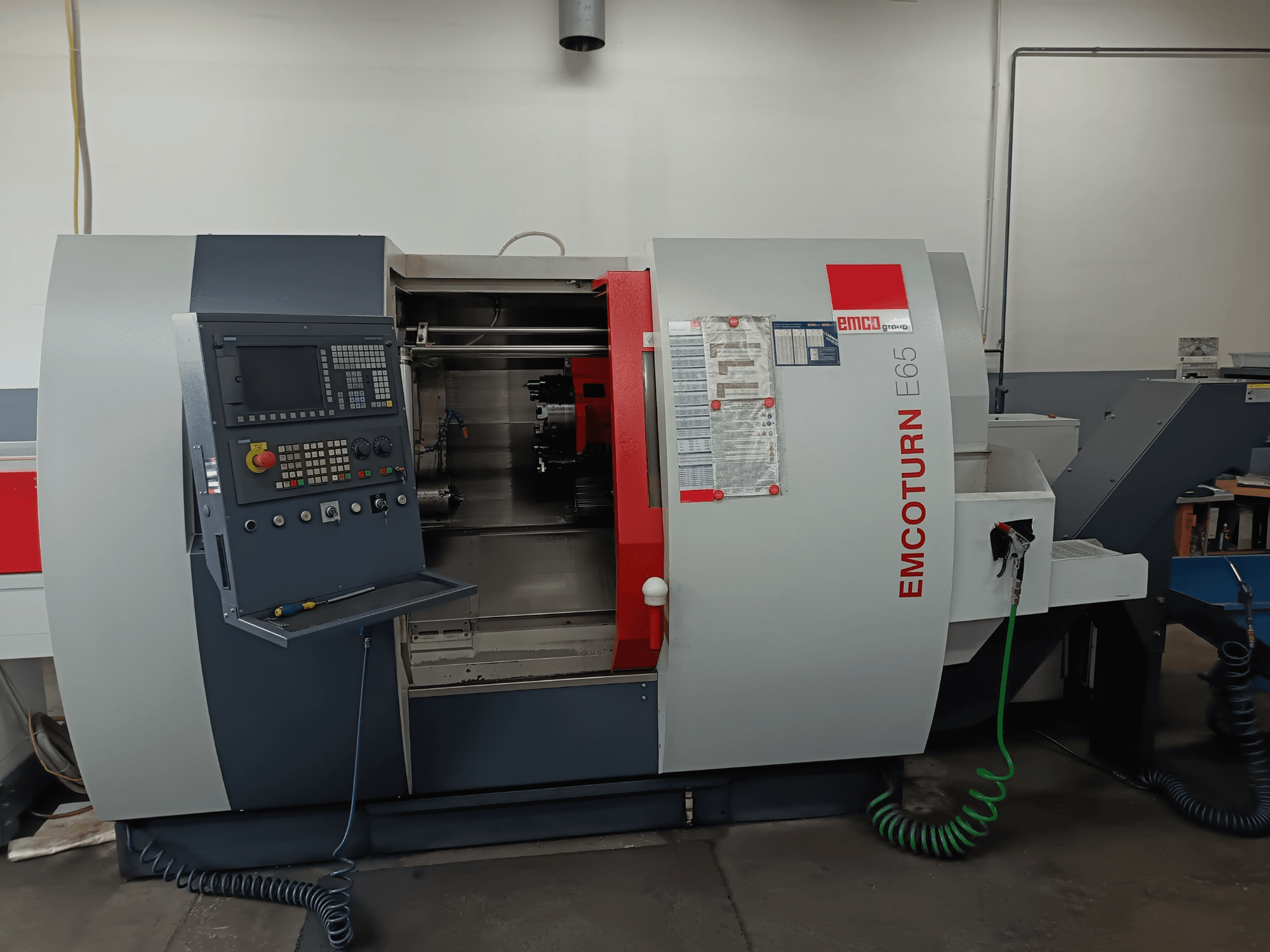 Soustružnické centrum EMCO EMCOTURN E65, čelní pohled zobrazující ovládací panel, vnitřní mechanismus a funkce v dílenském prostředí.