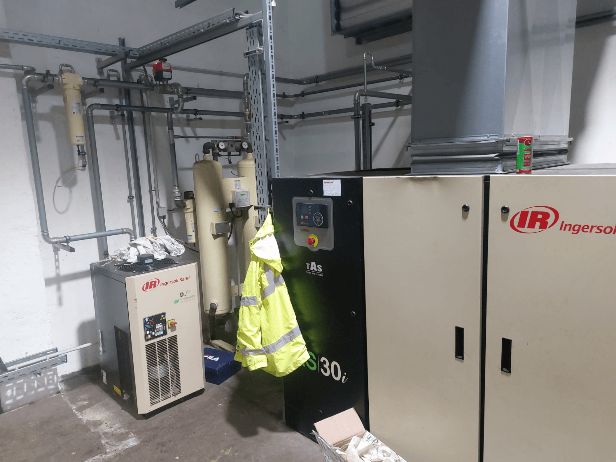Obráběcí stroj Ingersoll Rand D480EC-A v dílně, boční pohled s potrubím, ovládacími prvky a žlutou bezpečnostní vestou v blízkosti.