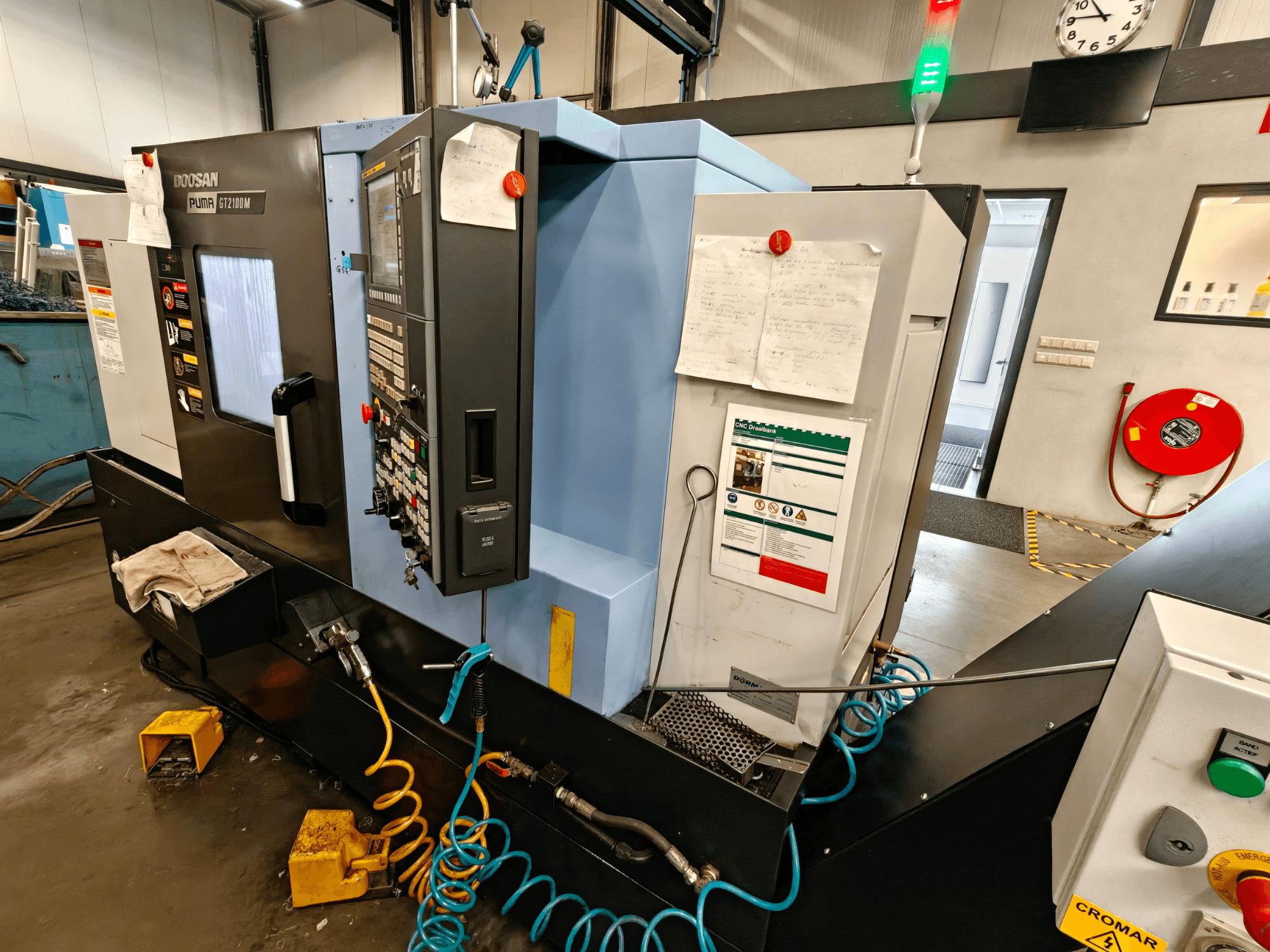 Pohled zepředu na horizontální soustruh DOOSAN Puma GT 2100M s viditelným ovládacím panelem, bezpečnostními prvky a poznámkami k údržbě.