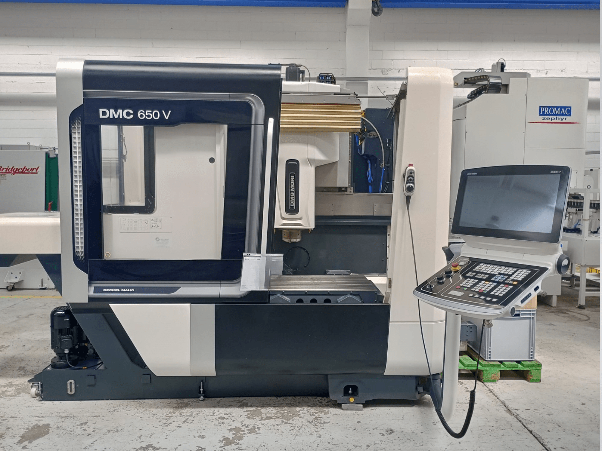 Boční pohled na CNC stroj Decker Maho DMC 650 V s ovládacím panelem s tlačítky a obrazovkou v průmyslovém prostředí.