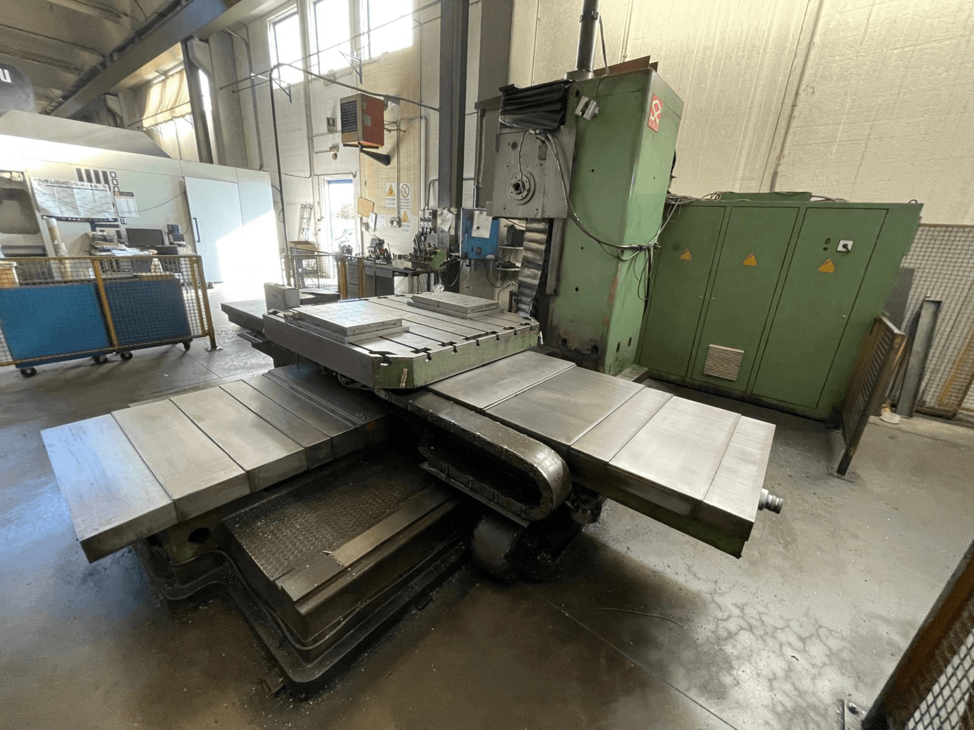 Velká průmyslová frézka se zelenou karoserií, pohled z boku, s několika rovnými plochami a úložnými skříněmi v pozadí.