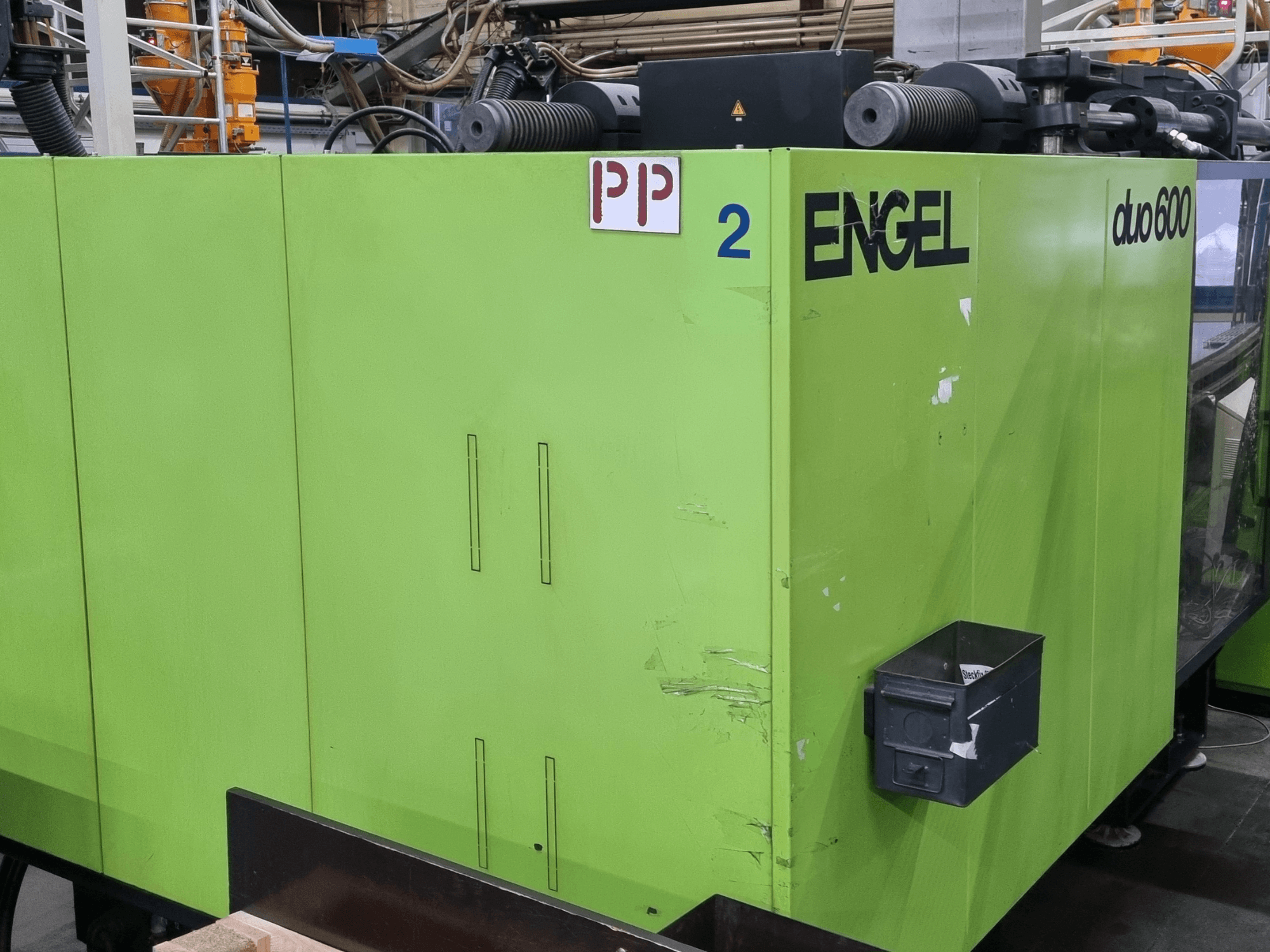 Hydraulický vstřikovací lis Engel Duo 600, zelený exteriér, pohled zepředu, s označenými součástmi a úložným boxem na materiál.