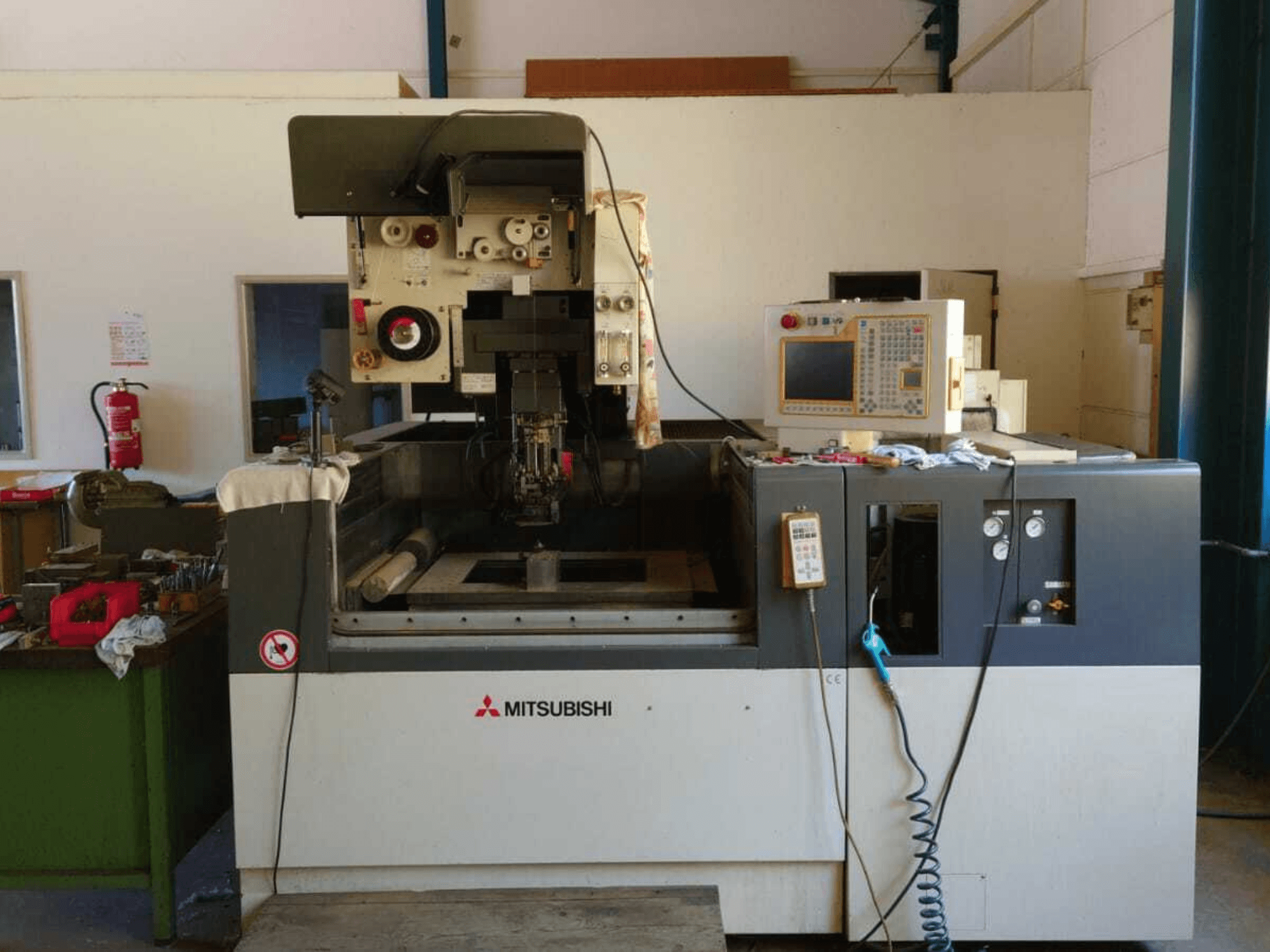 Pohled zepředu na drátovou elektroerozivní frézu Mitsubishi FA20, na kterém je vidět ovládací panel, pracovní prostor a bezpečnostní značení.