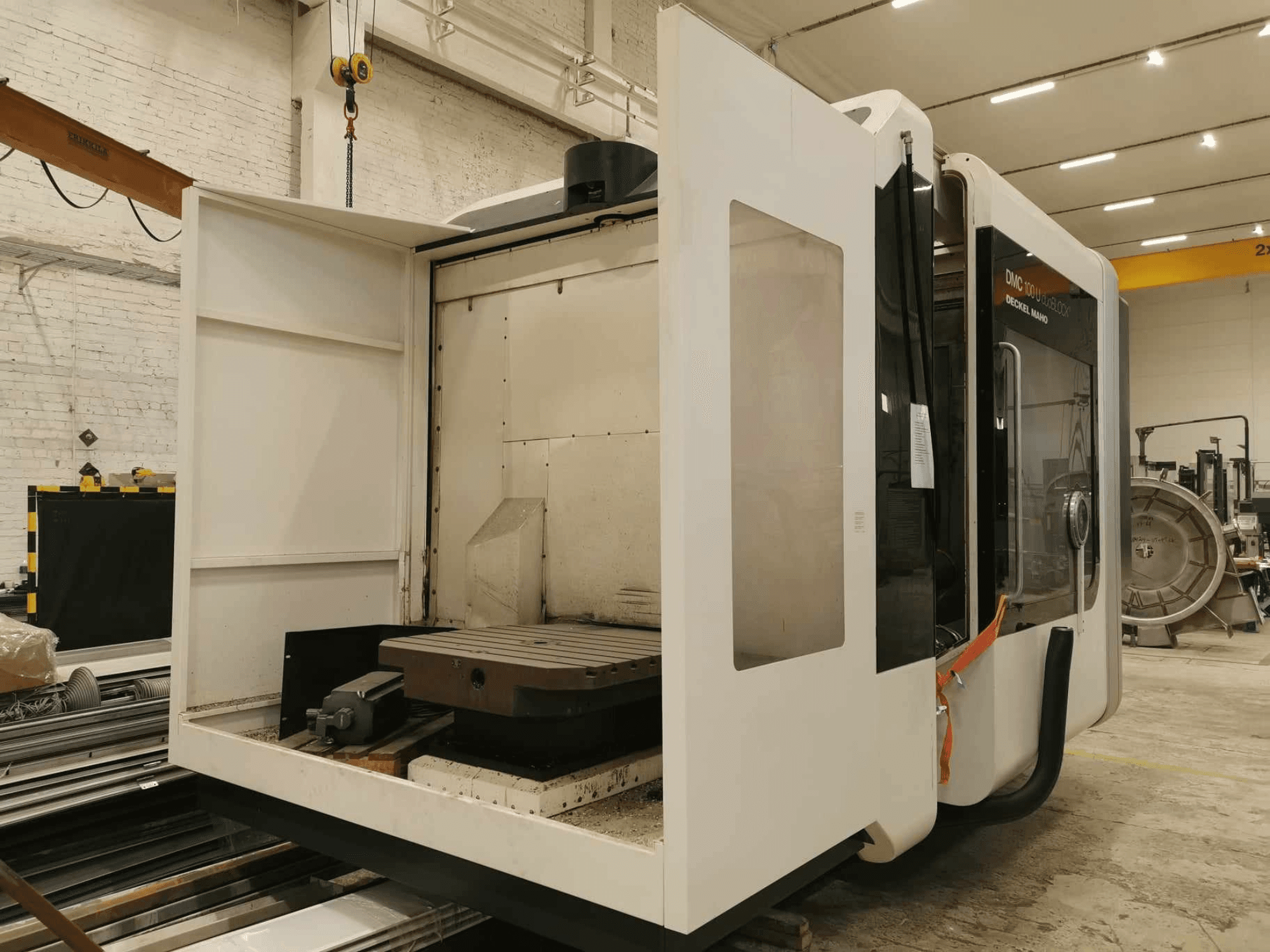 Lineární CNC stroj DMC 100U, boční pohled s otevřenými přístupovými dvířky, zobrazující pracovní stůl a vnitřní komponenty.