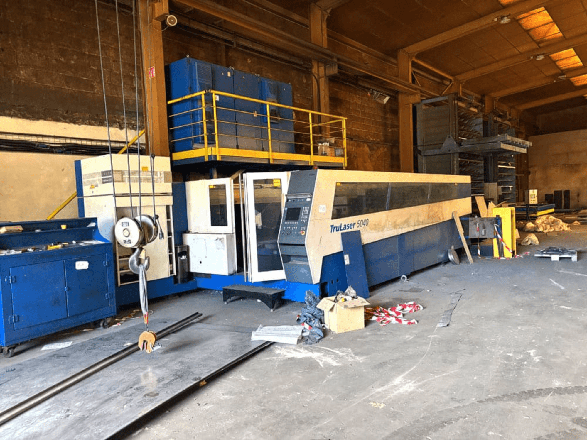 Stroj na řezání CO₂ laserem od společnosti TRUMPF, model TRULASER 5040, zachycený v dílně, šikmý čelní pohled s přeplněným pozadím.