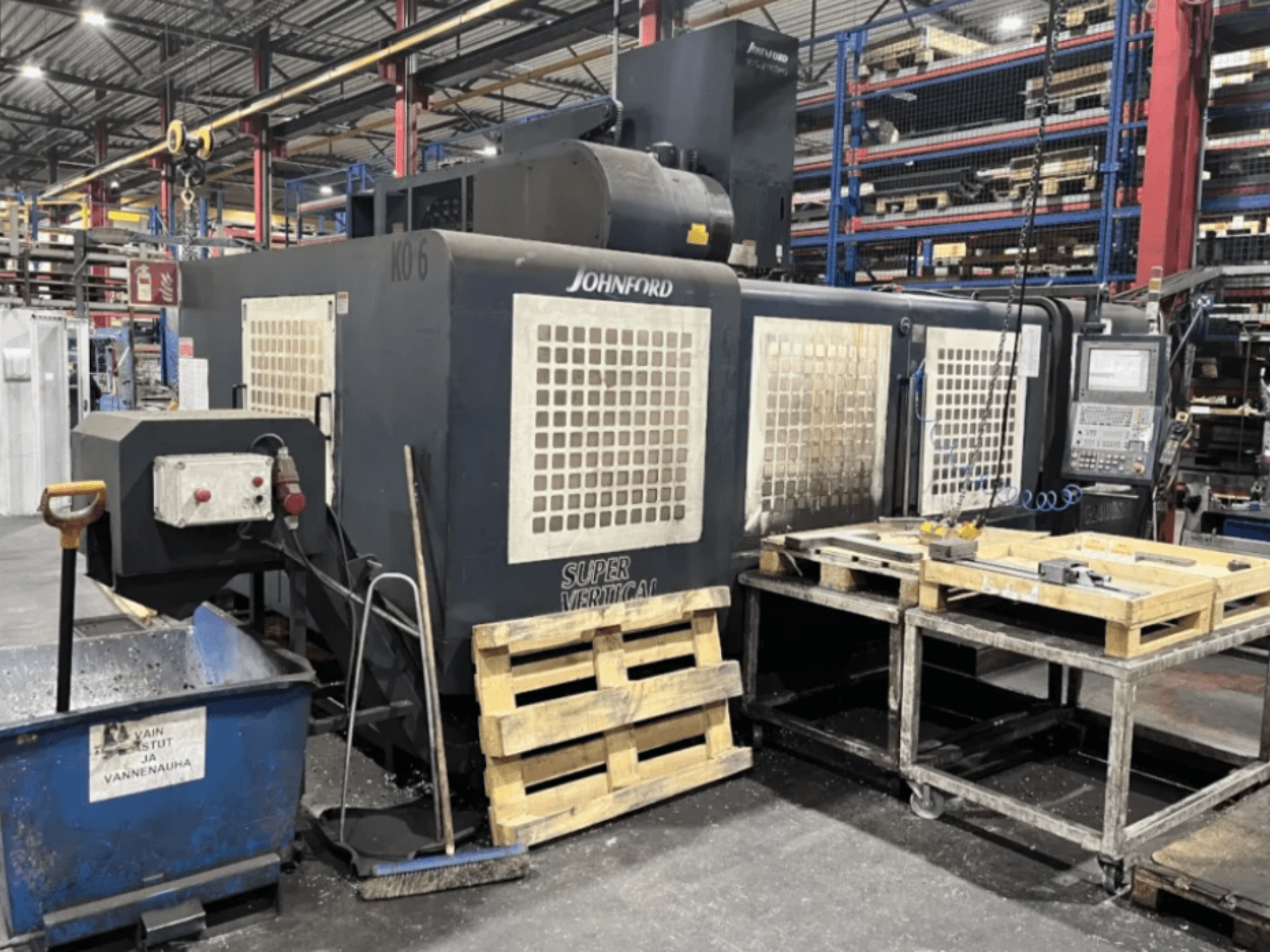 Super vertikální frézka Johnford v továrně, boční pohled s ovládacím panelem, paletami a čisticím zařízením v blízkosti.