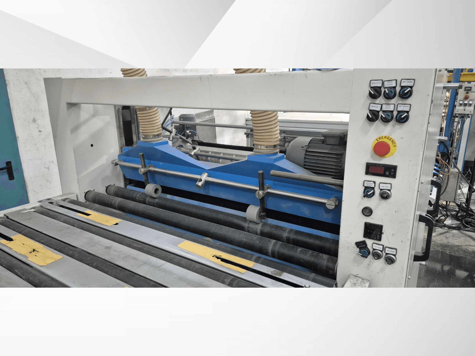 Průmyslový válcovací stroj s modrými komponenty, pohled zepředu, s ovládacím panelem a tlačítkem nouzového zastavení.