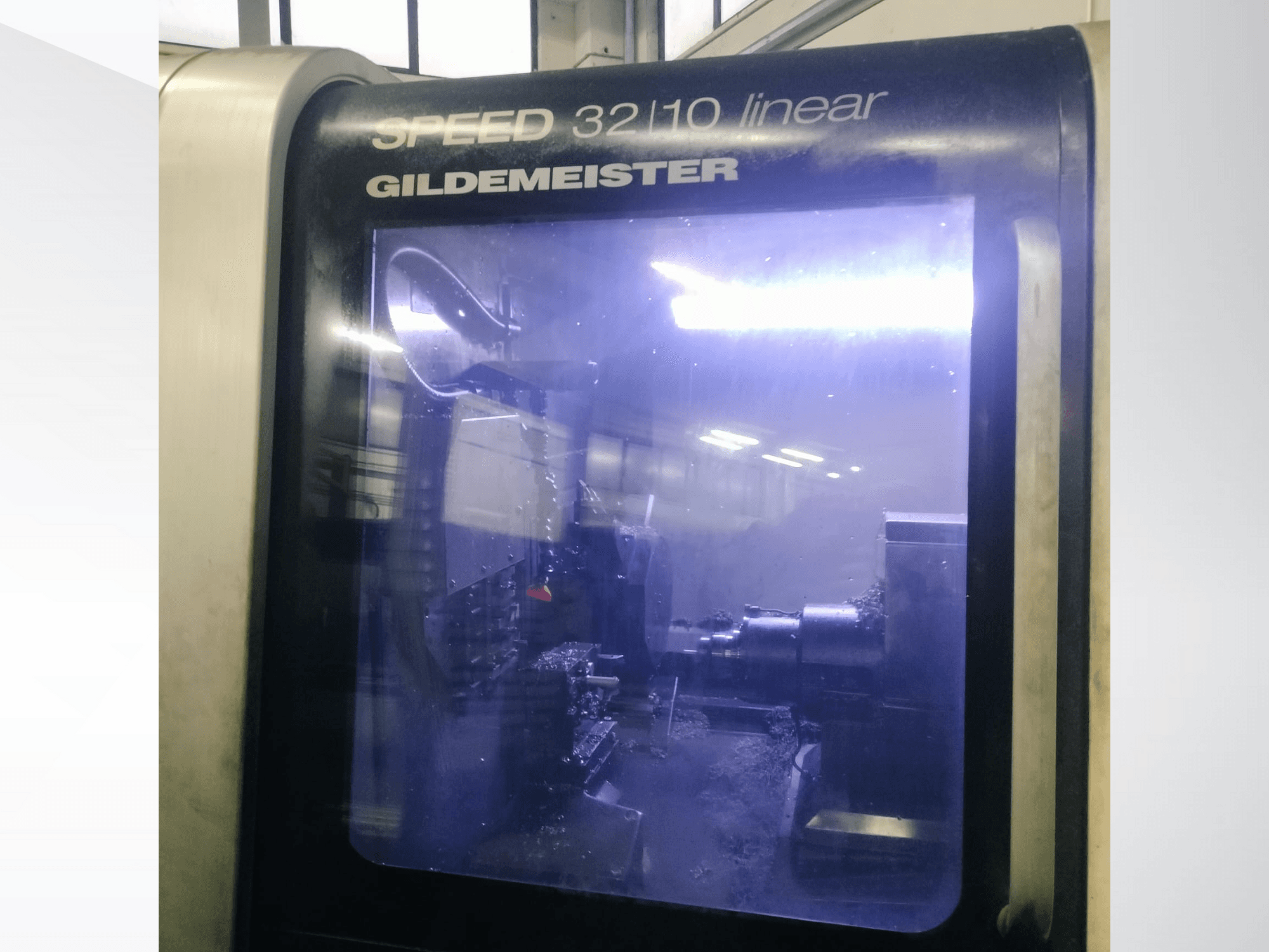 Pohled zepředu na lineární CNC stroj Gildemeister SPEED 3210, zobrazující vnitřní komponenty a kapalné chladicí médium v provozu.