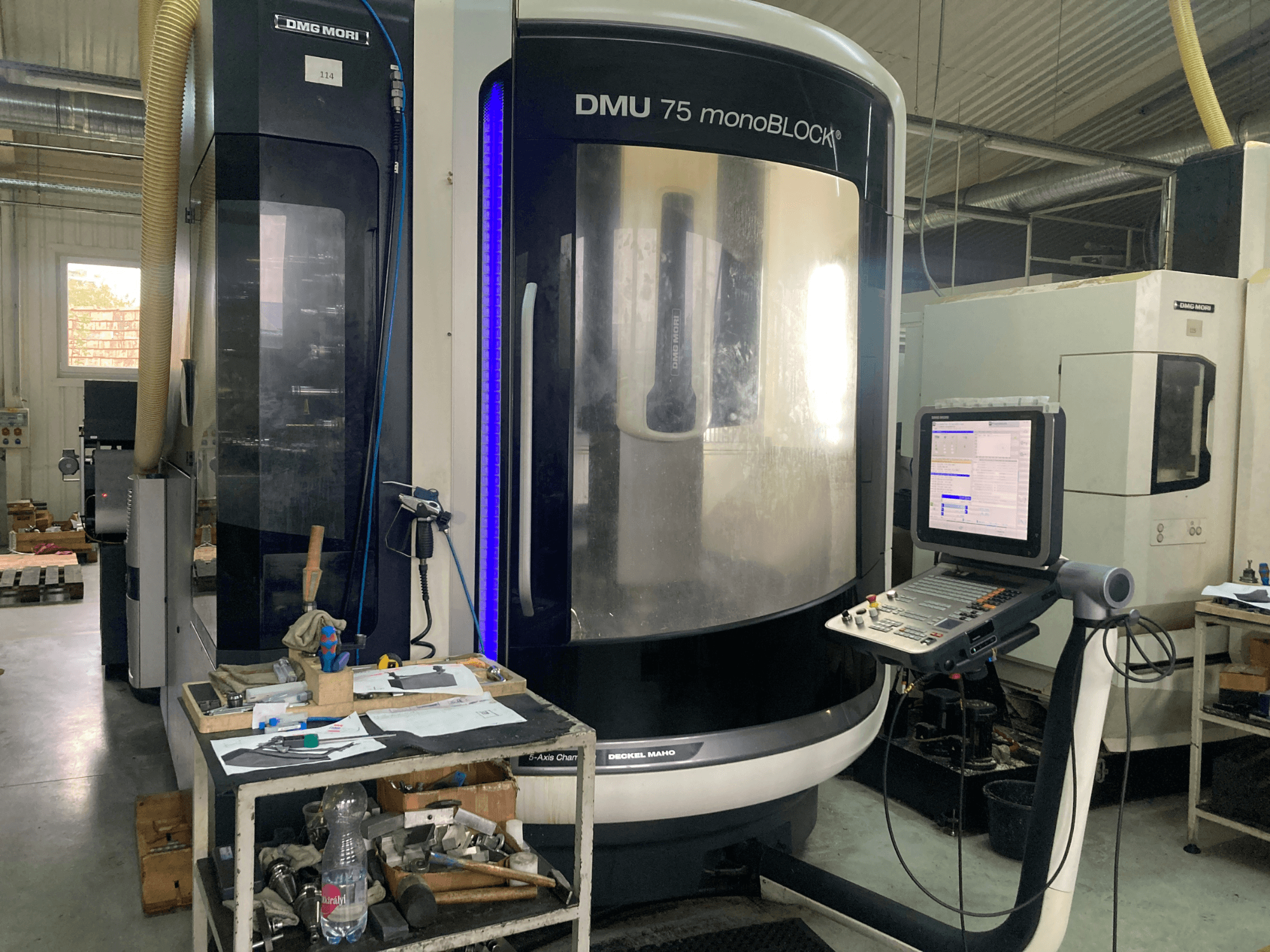 Stroj DMG MORI DMU 75 monoBLOCK® CNC, pohled zepředu, s ovládacím panelem, nástroji a pracovním prostorem s materiály.