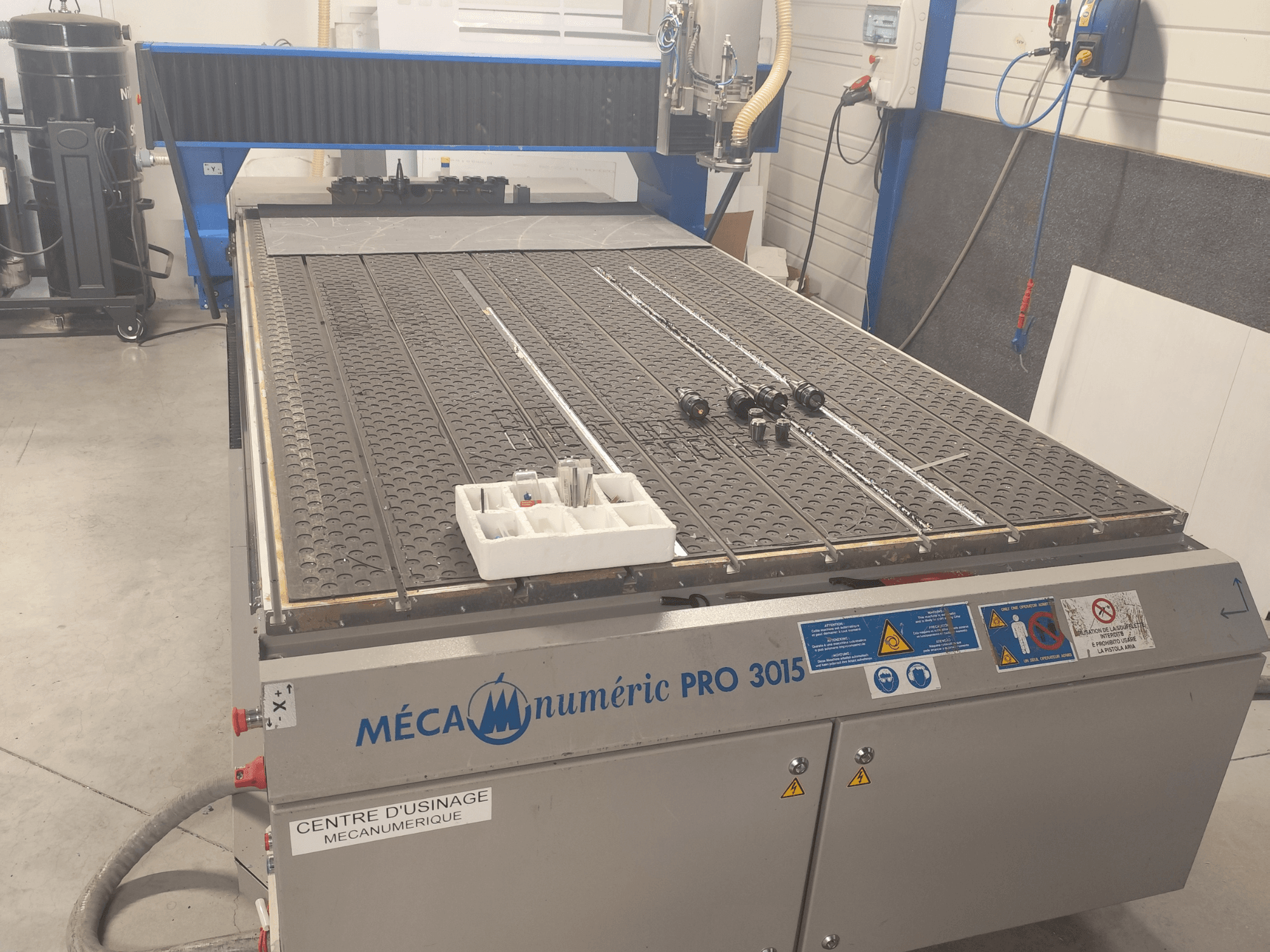 CNC frézka MECANUMERIC Pro 3015 – pohled zepředu, na kterém je vidět detailně zpracovaný řezací stůl, ovládací panel a příslušenství na stole.