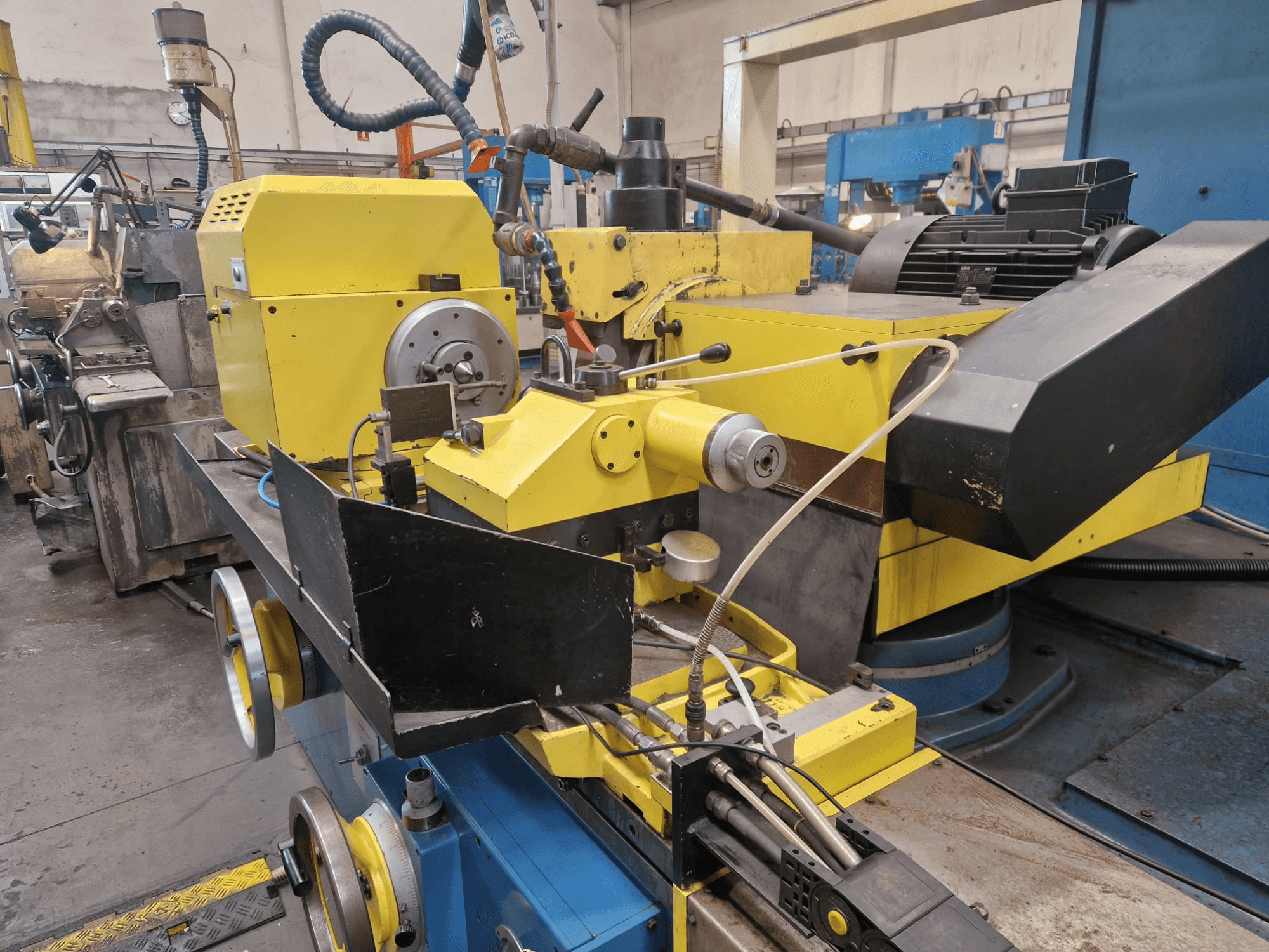 Žlutý průmyslový stroj s černou částí s číselníkem a hadicemi, pohled zepředu pod mírným úhlem.