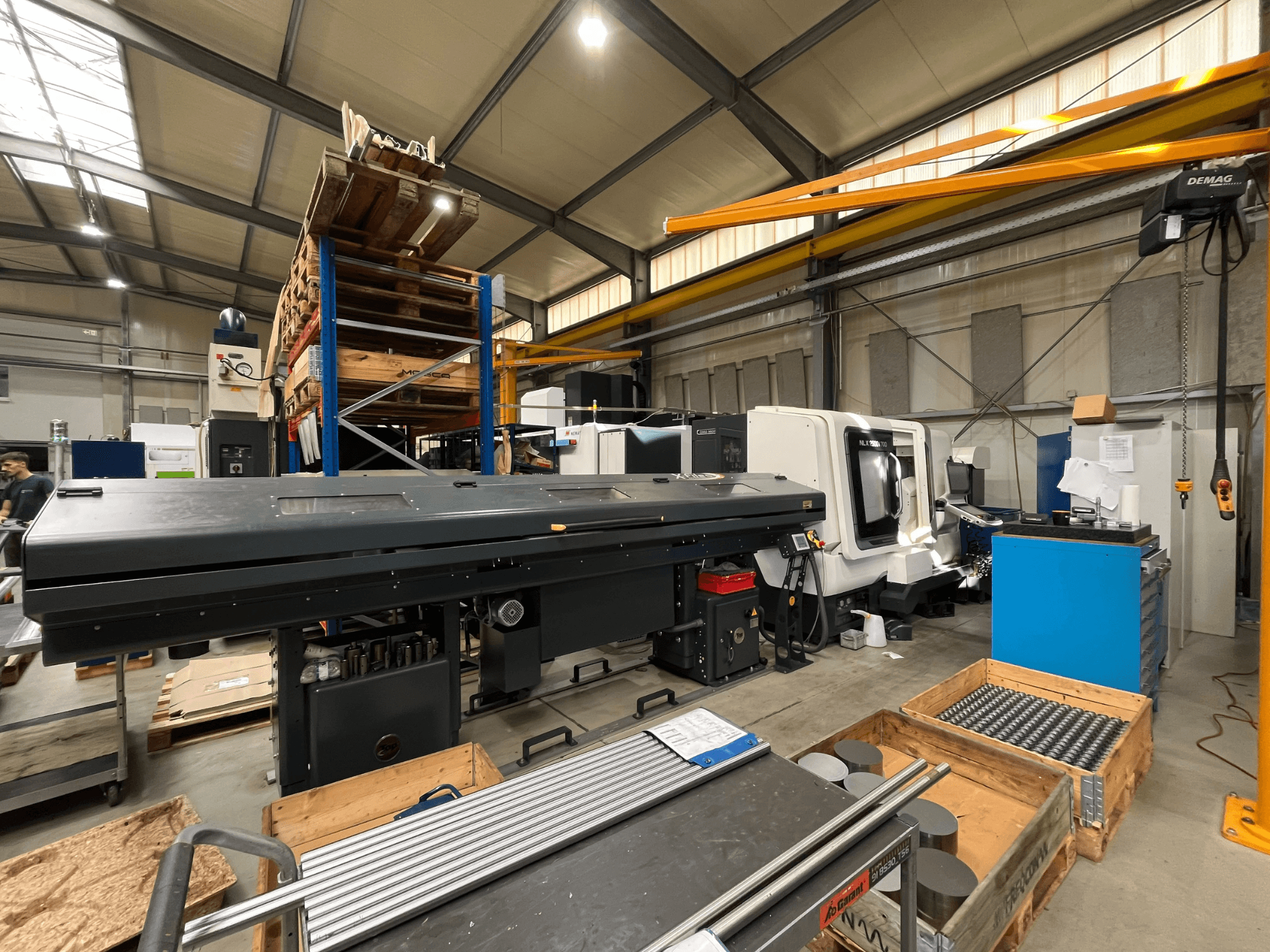 Horizontální soustruh DMG MORI MORI NLX 2500/700 SY v dílně, pohled z boku, v pozadí je vidět sklad a nářadí.