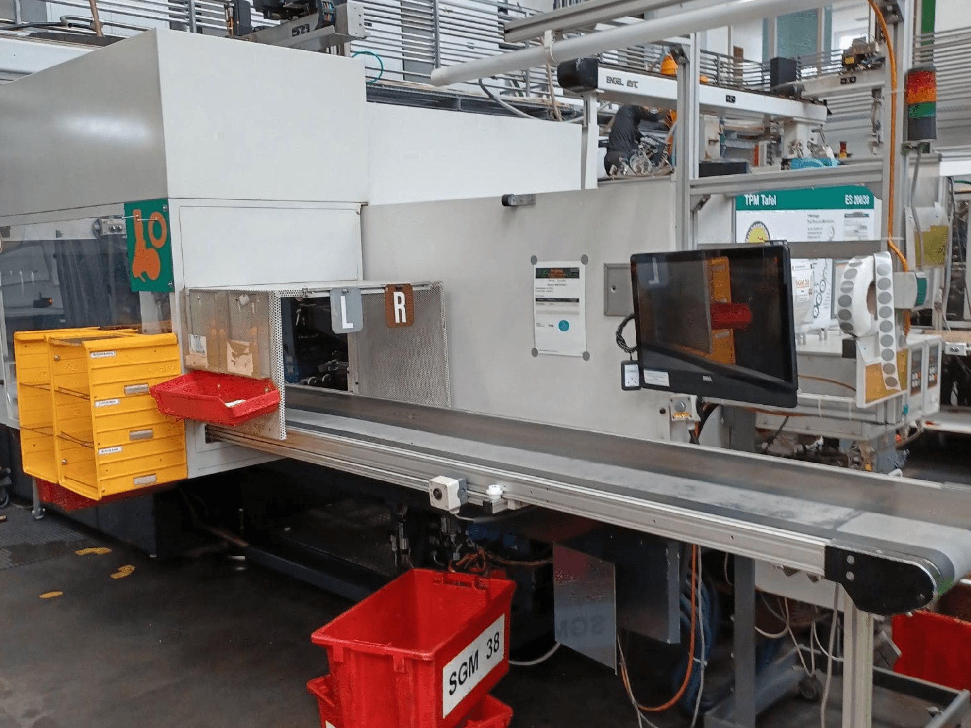 Průmyslový třídicí stroj se žlutými a červenými zásobníky, pohled z boku, s kontrolním monitorem a označenými přihrádkami pro třídění.