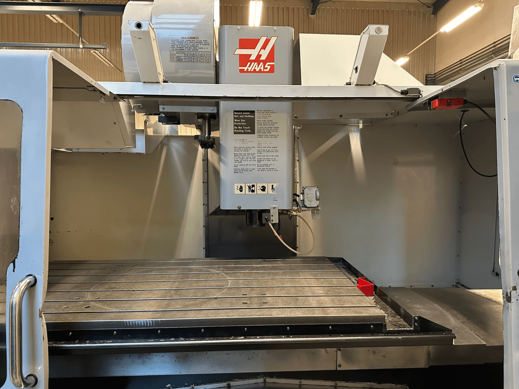 CNC frézka Haas, model VF-2, pohled zepředu, kde jsou vidět ovládací prvky, kovový pracovní stůl a bezpečnostní štítek na panelu.