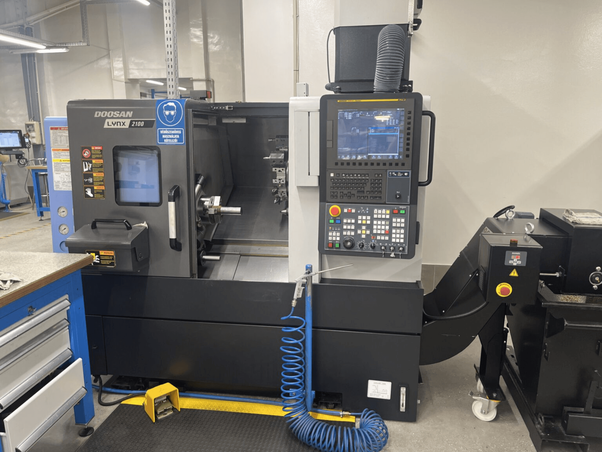 Pohled zepředu na horizontální soustruh DOOSAN Lynx 2100A, na kterém je vidět ovládací panel a prostor vřetena s pozoruhodnými bezpečnostními prvky.