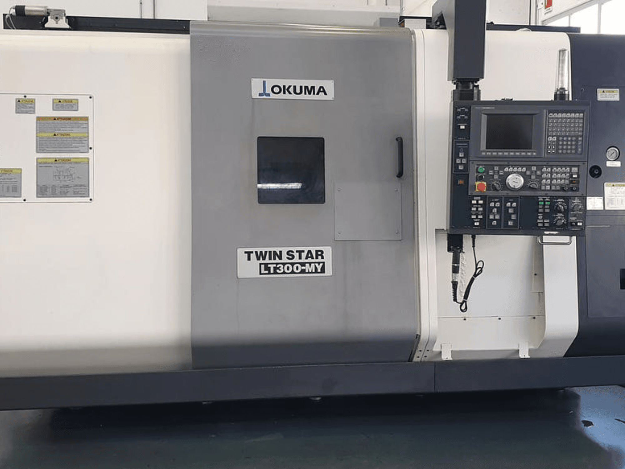 CNC soustruh Okuma Twin Star LT300-MY v bočním pohledu, s ovládacím panelem, provozními tlačítky a bezpečnostními štítky.