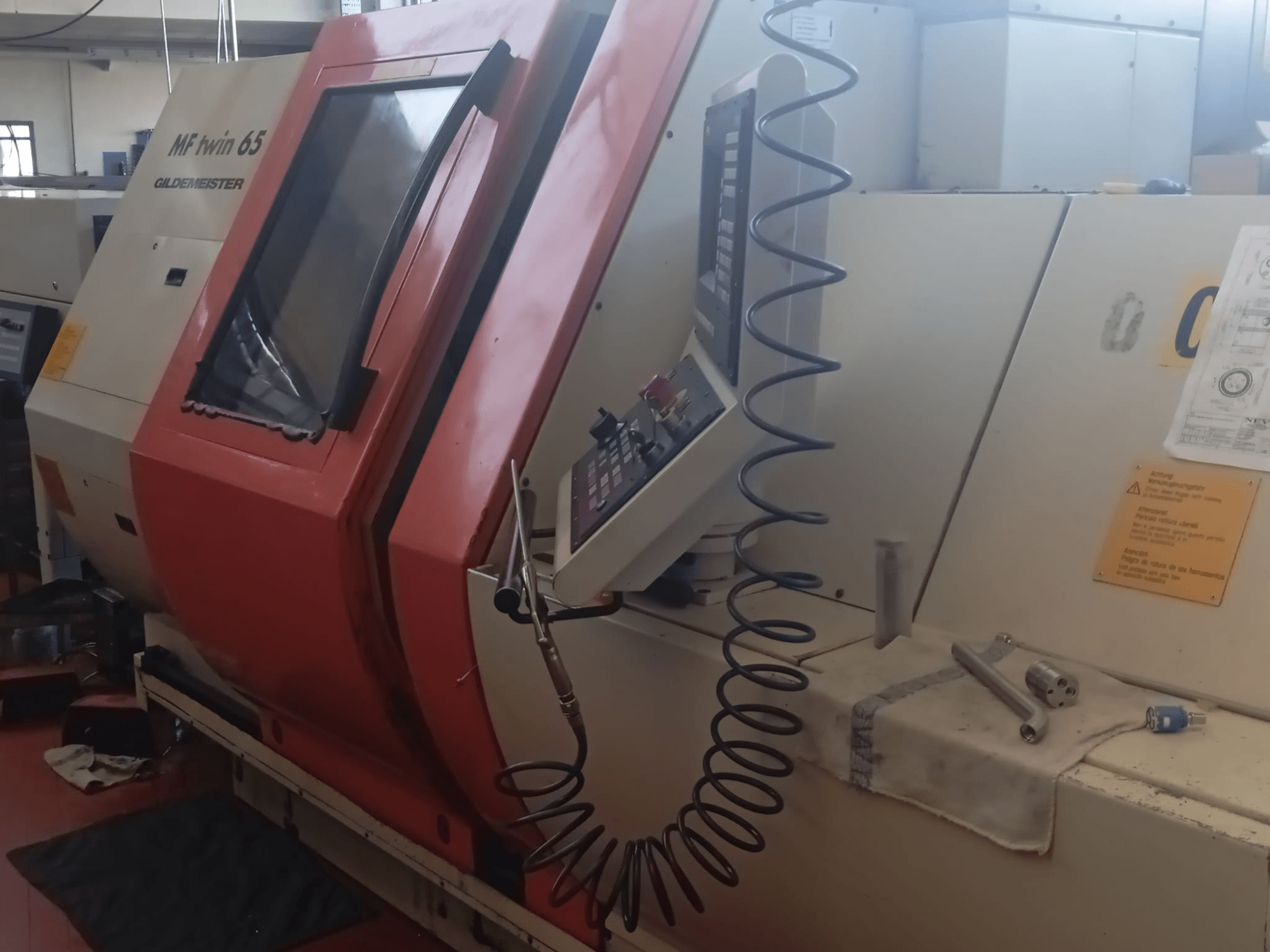 Oranžovo-bílý stroj MF twin 65 Gliedemeister, pohled zepředu, s ovládacím panelem a nástroji na plátně.