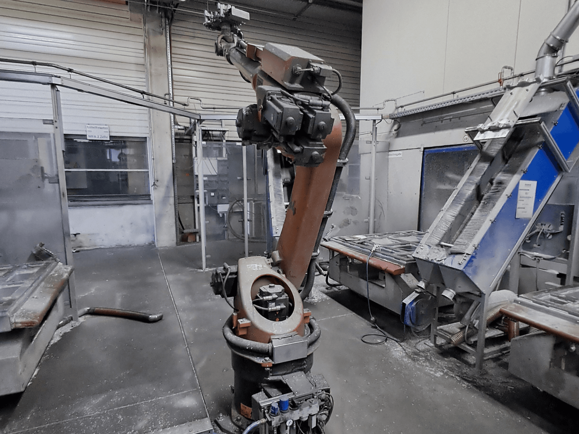 Robotické rameno KUKA KR 30L16-2 v dílenském prostředí, pohled zepředu, v pozadí je vidět prach a strojní zařízení.