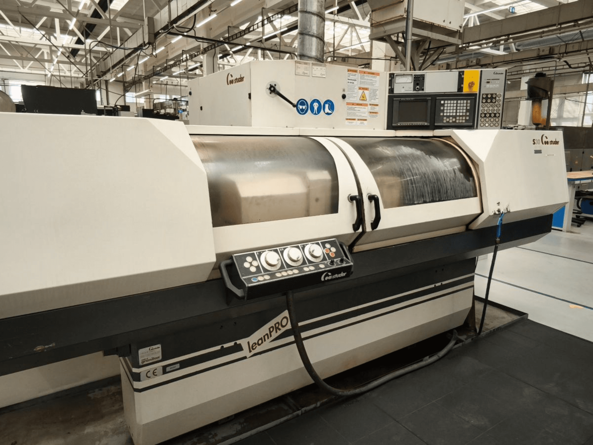 Bruska na kulato STUDER S30 LEAN PRO, boční pohled na ovládací panel a kryt brusného kotouče v průmyslovém prostředí.