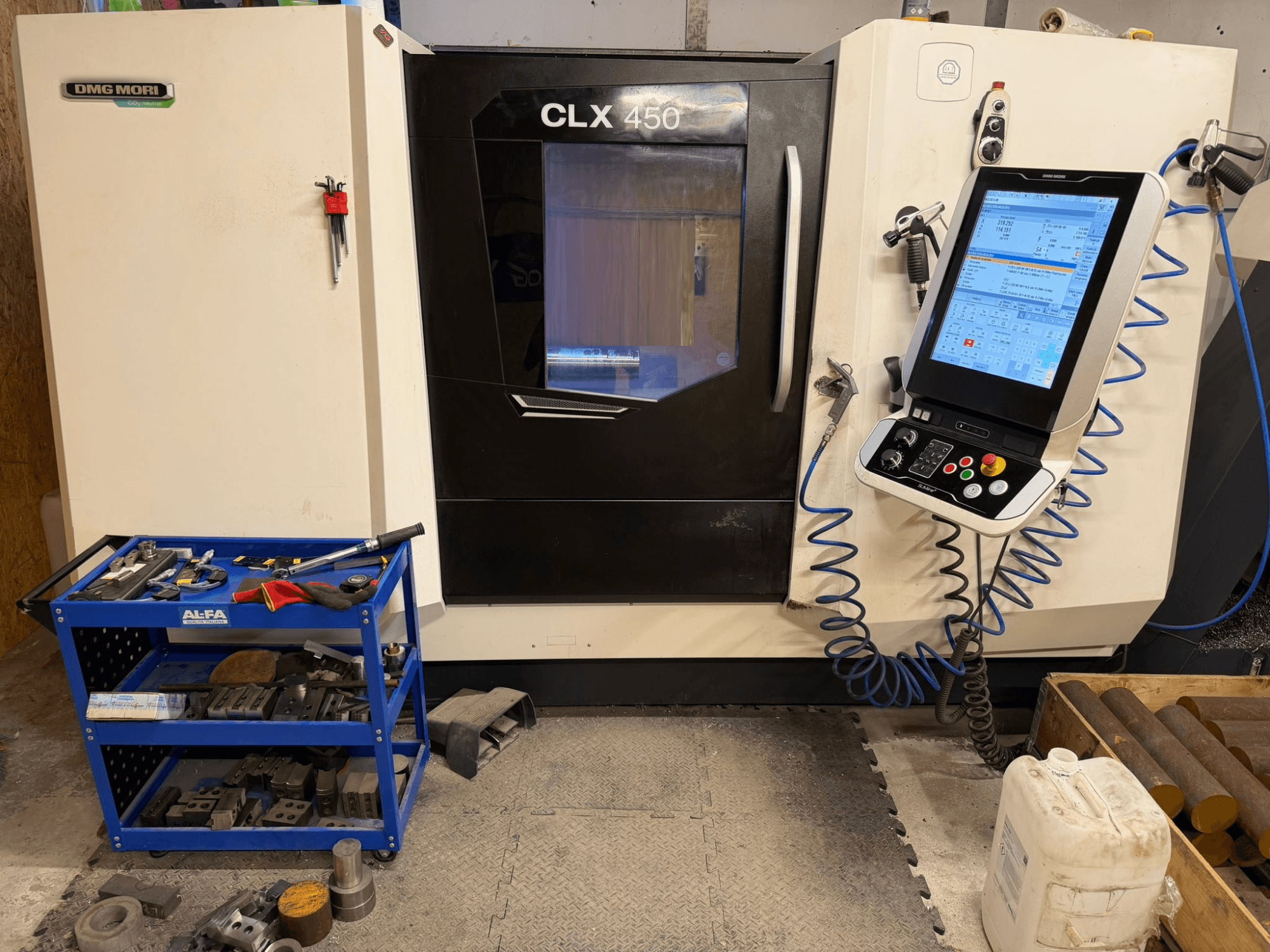 Pohled zepředu na horizontální soustruh DMG MORI CLX 450 V3 s ovládacím panelem a nedalekým vozíkem s nářadím.